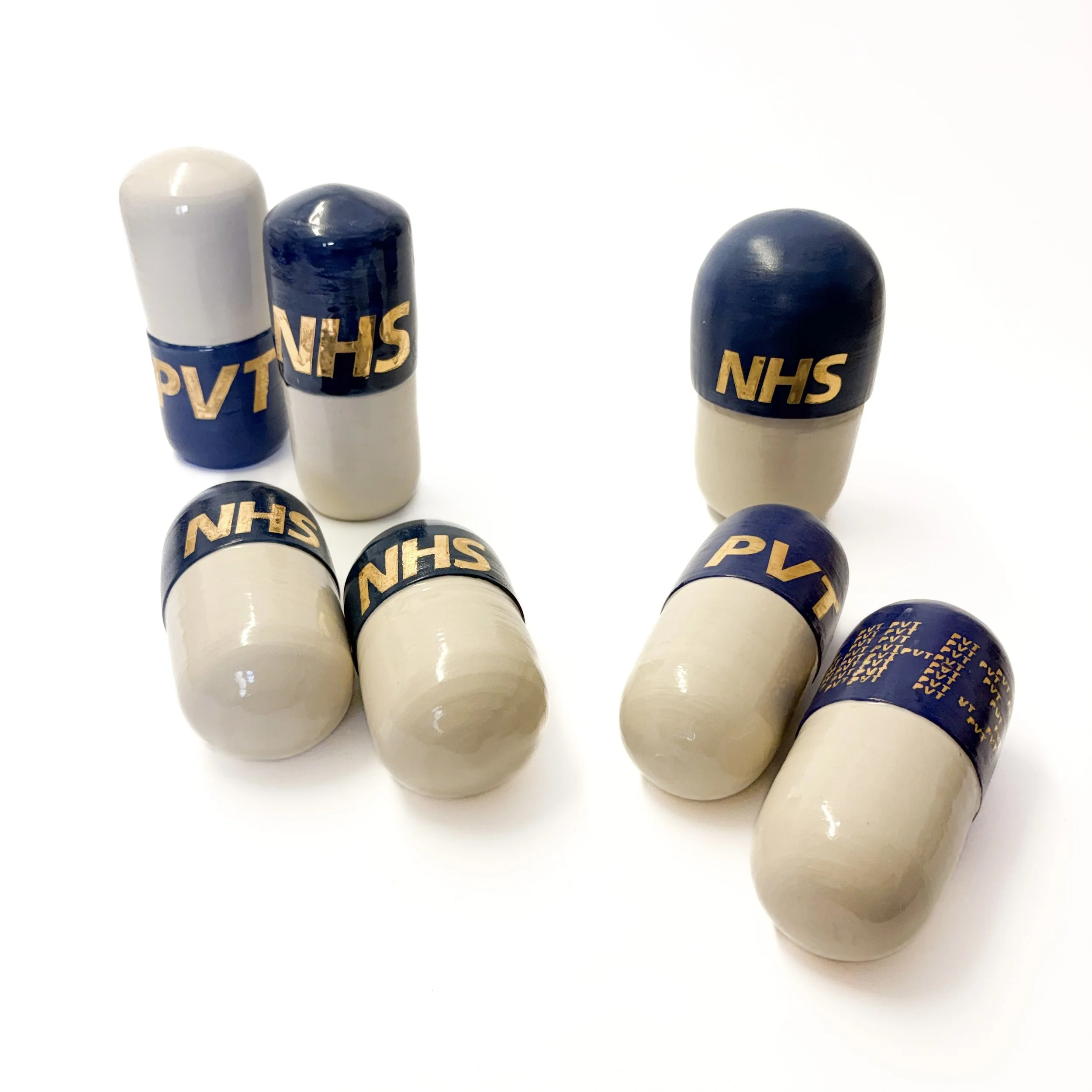 Several medicine capsules with 'NHS' printed on their blue and white body, lying on a white surface.