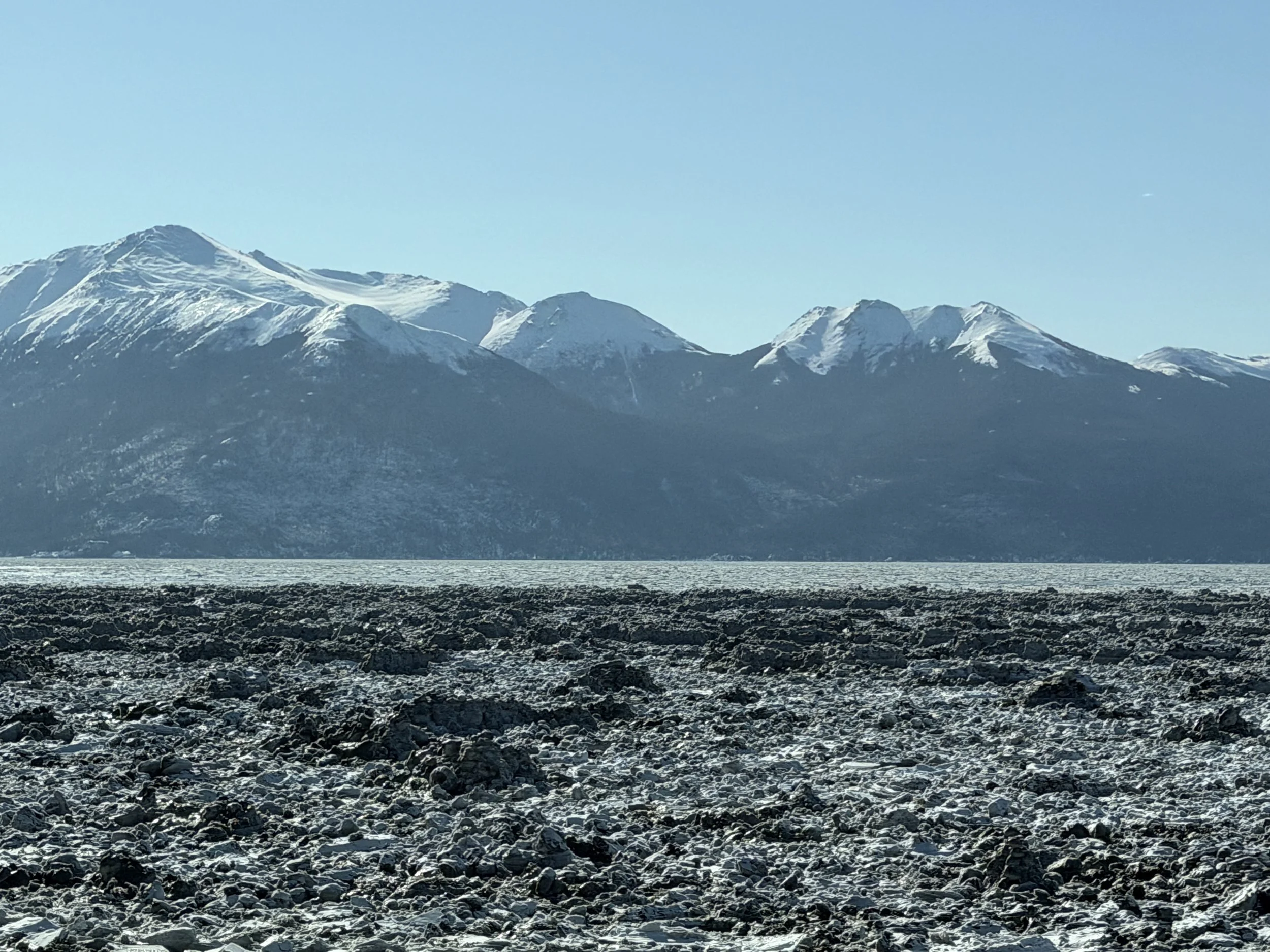   Low tide in Turnagain Arm. With its extreme tidal ranges (~38ft or 11.5m) and freezing temperatures, the water freezes around mud and sediment creating dirty looking, rounded ice chunks lumped into large piles along the shoreline.  