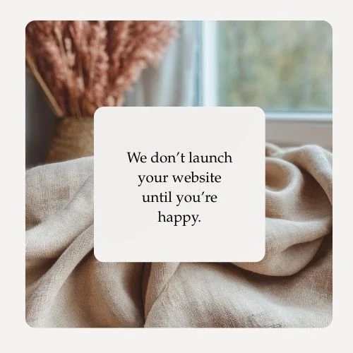 A white square with black text that says, "We don’t launch your website until you’re happy," placed on a beige fabric with a window and a vase of dried flowers in the background.