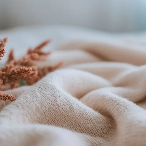 Close-up of soft, cream-colored fabric with a blurred background and some pinkish decorative plants.
