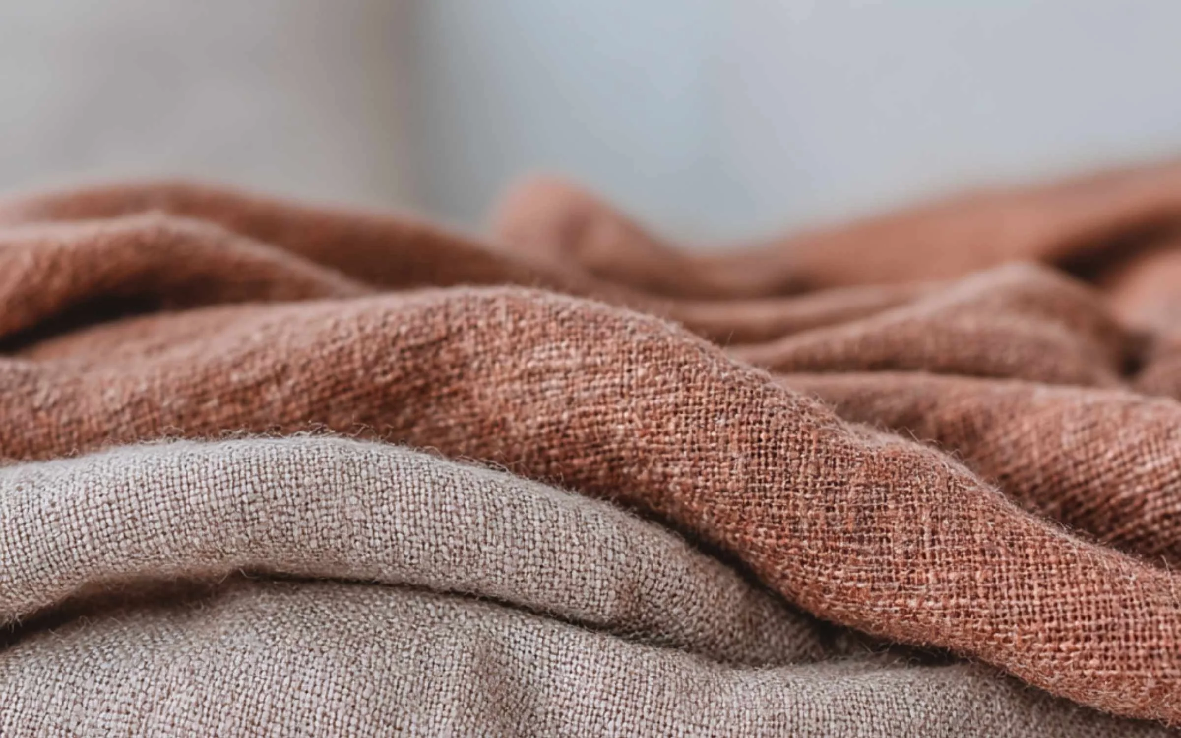 Close-up of textured fabric in muted earthy tones, showing the weave and soft folds.