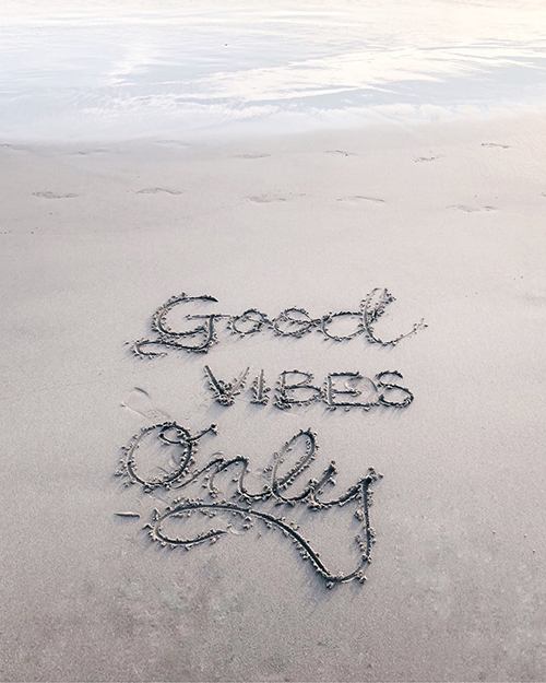 "Good Vibes Only" carved into the sand on a beach