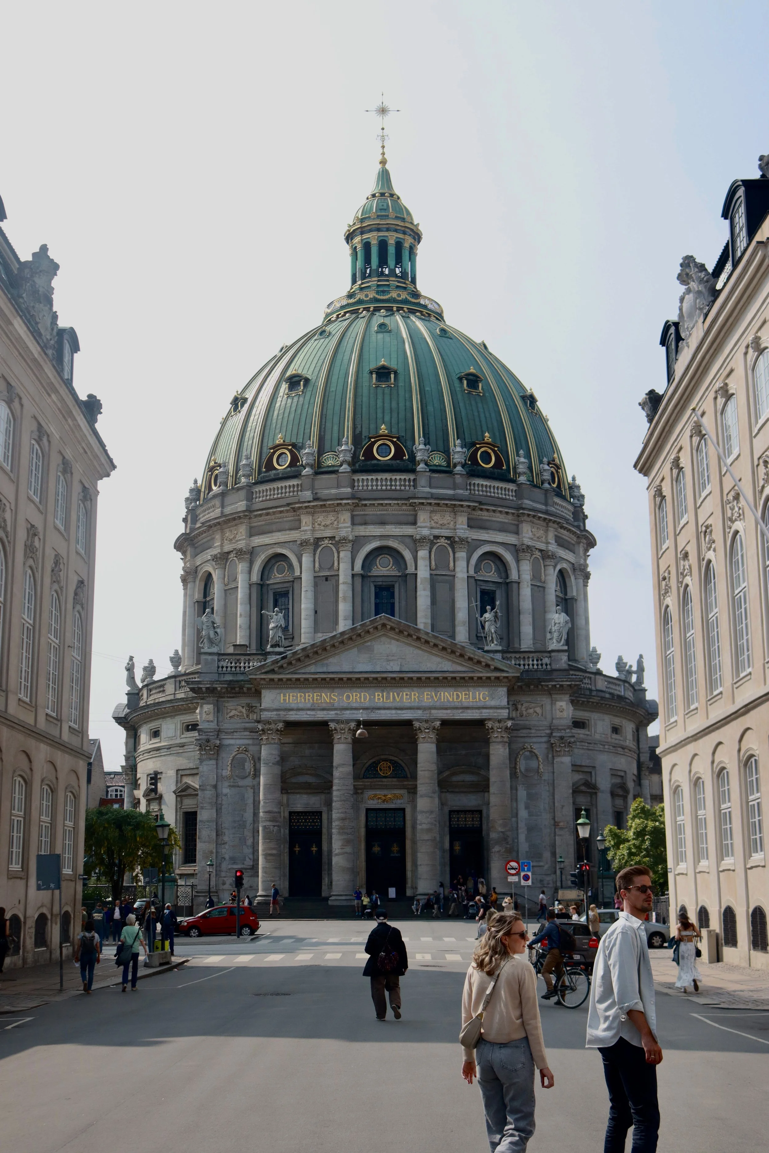 The image shows a large historical church with a green dome and ornate architecture, surrounded by a city street with pedestrians.