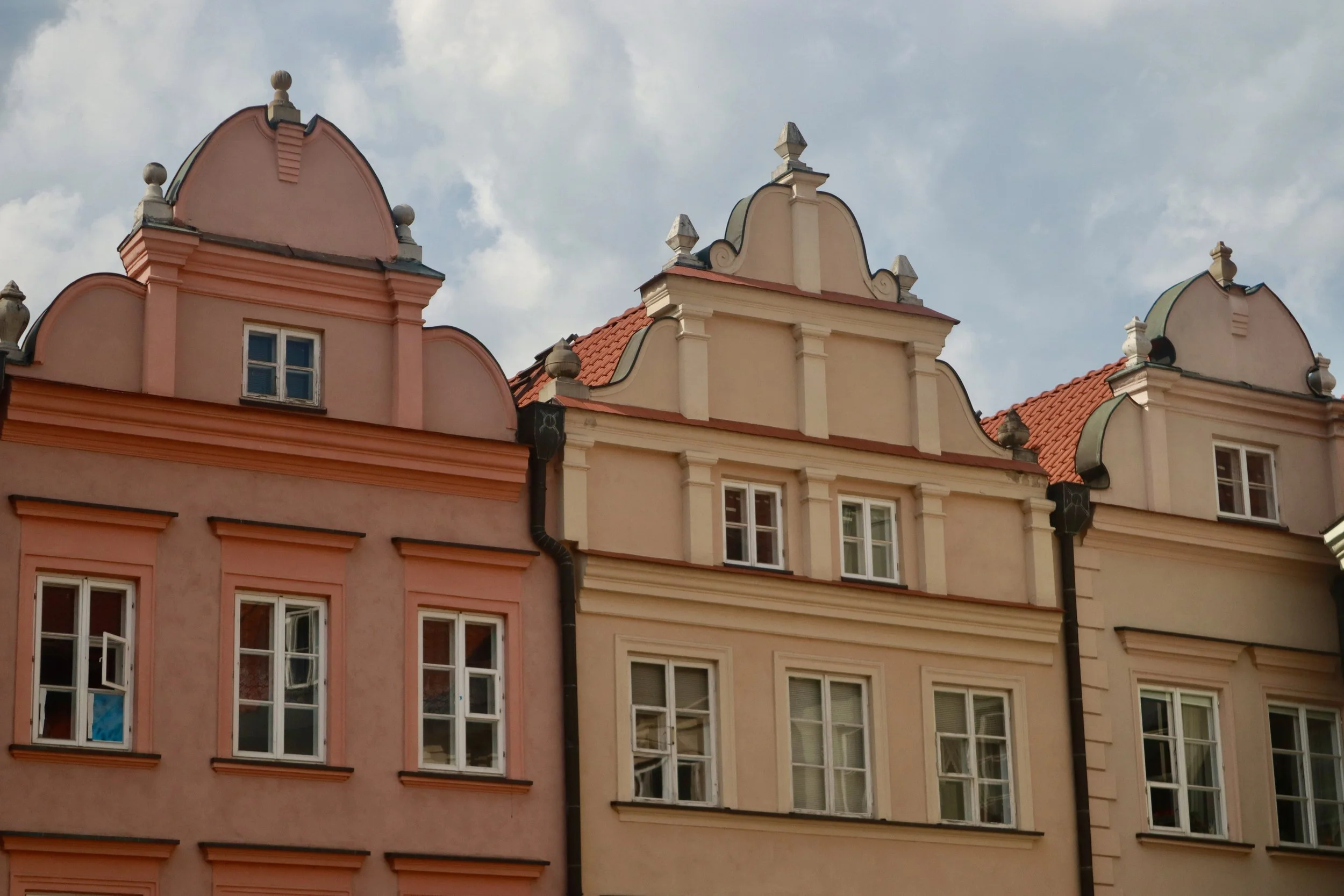 Colorful European-style buildings with ornate rooftop details and multiple windows against a cloudy sky.