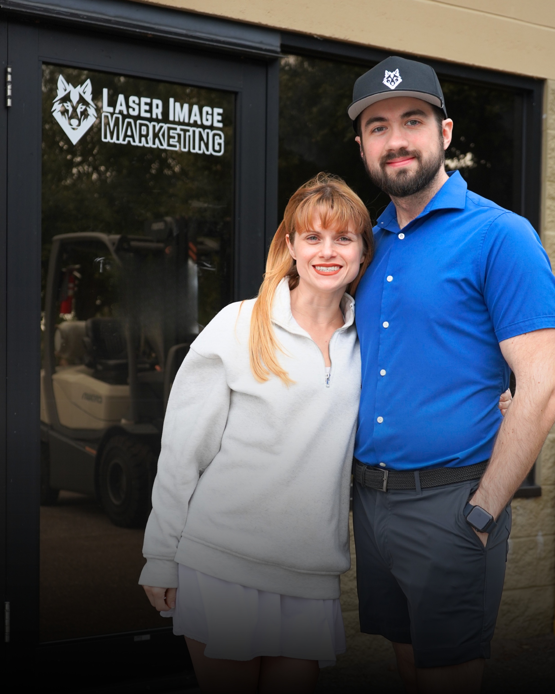 Two smiling people standing in front of a door with a sign reading 'Laser Image Marketing'.