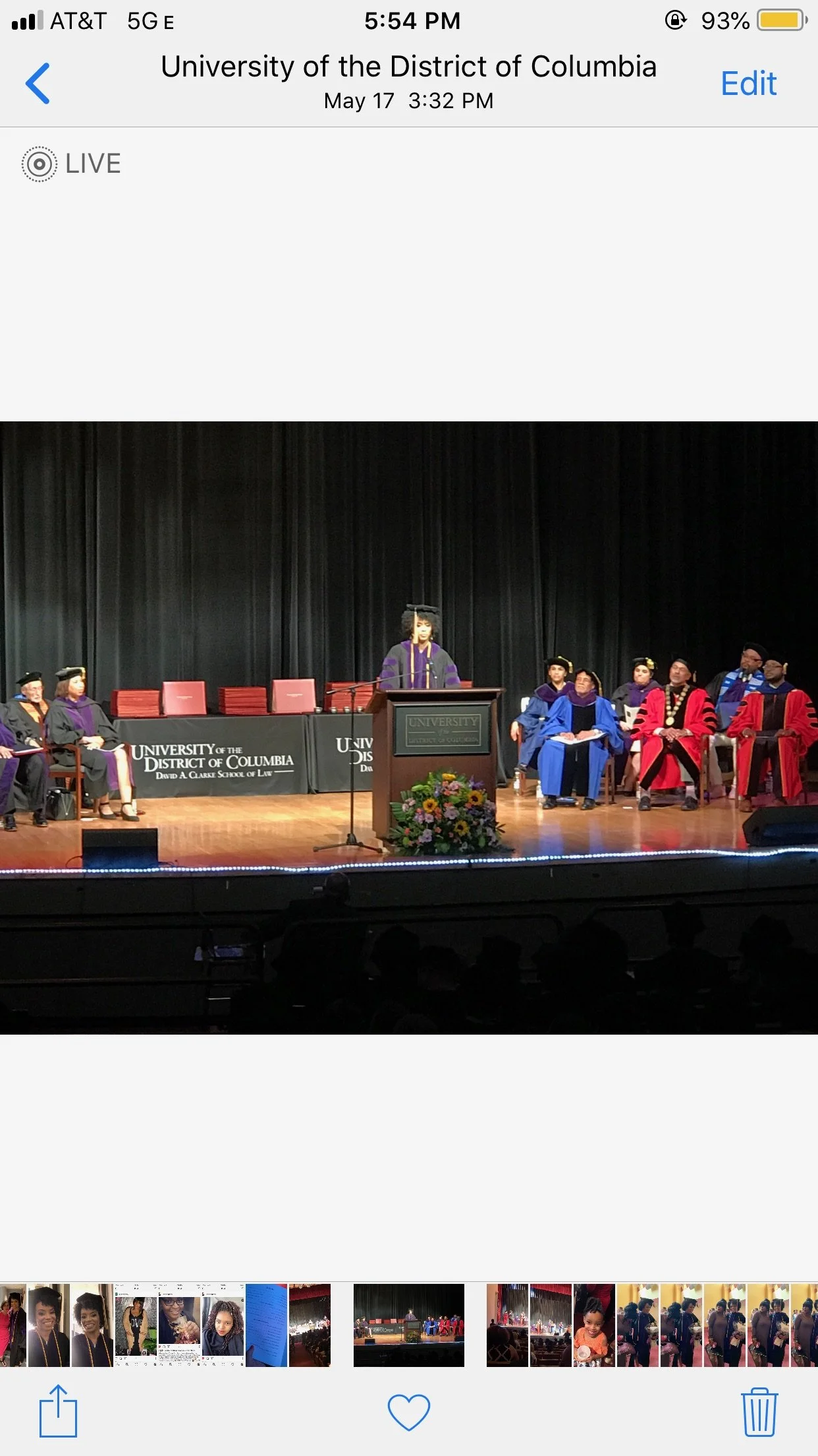 Graduates and faculty members seated on stage during a graduation ceremony at the University of the District of Columbia, with Amber Ivey speaking at a podium and a floral arrangement in front.