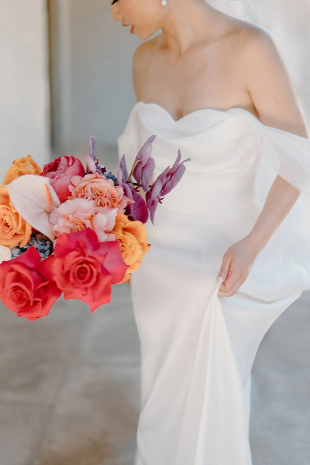 A woman in a white strapless gown holding a vibrant bouquet of pink, orange, purple, and peach flowers.