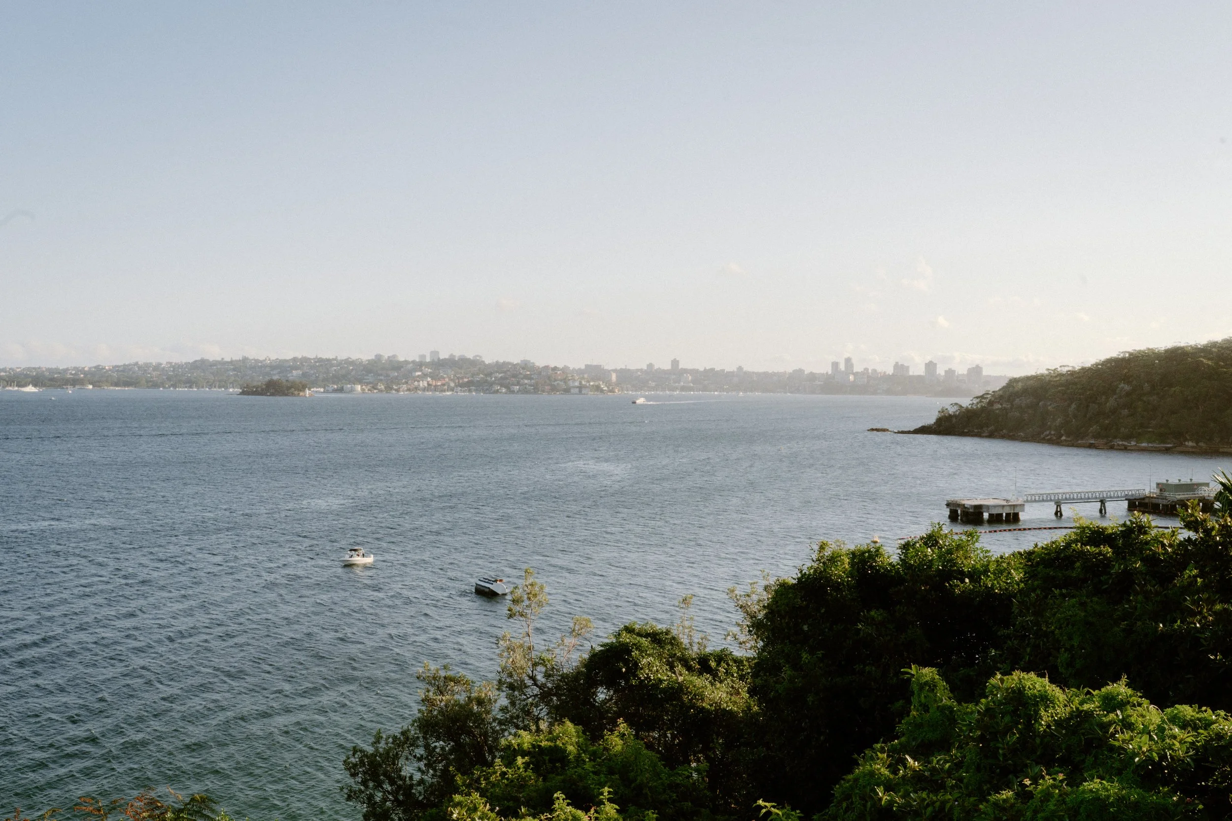Sergeants Mess, Mosman Wedding Venue. Sergeants Mess Wedding Photos. A body of water with boats, trees, and a distant city skyline on the horizon.