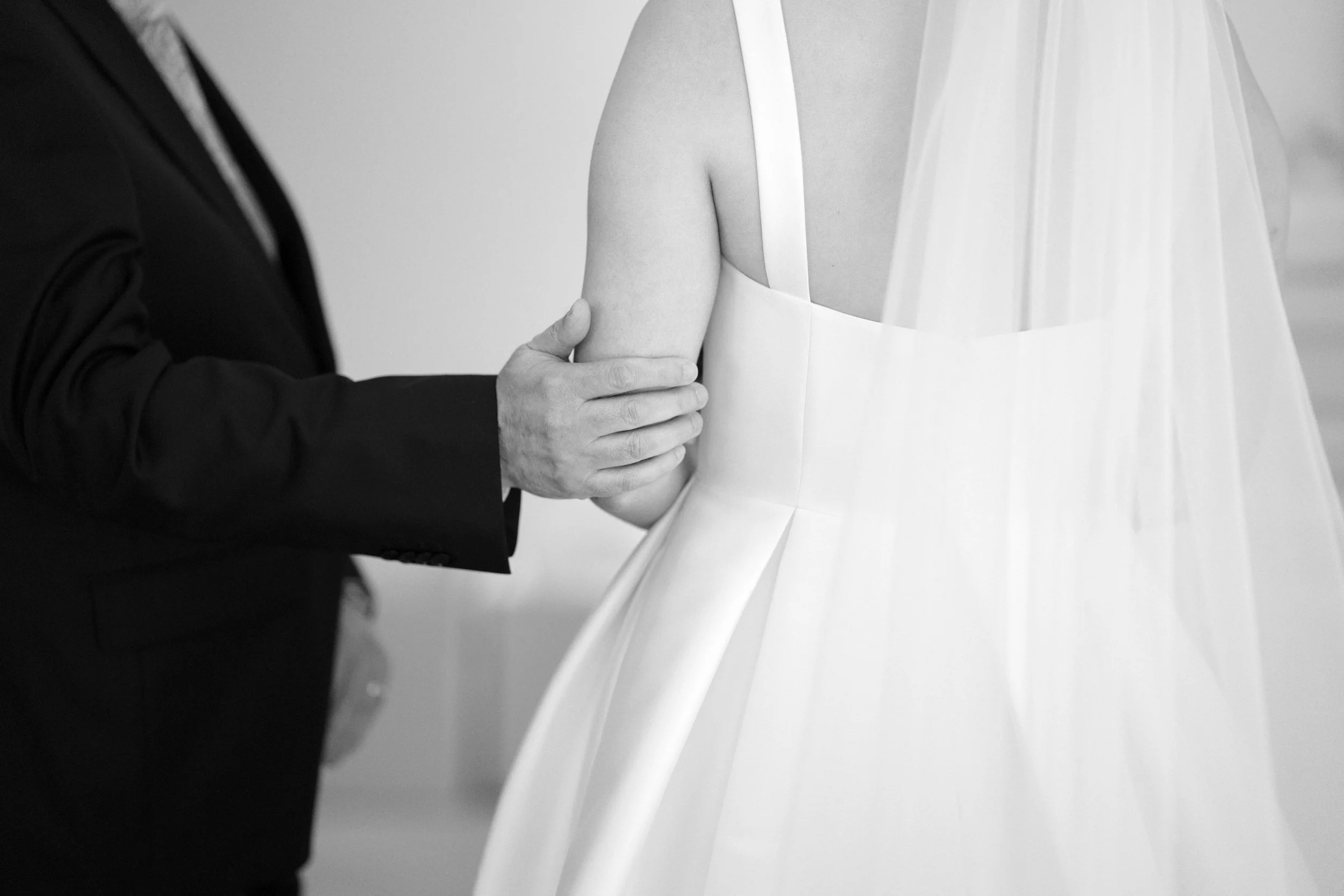 A person in a black suit holds the arm of a woman in a white wedding dress as they dance.