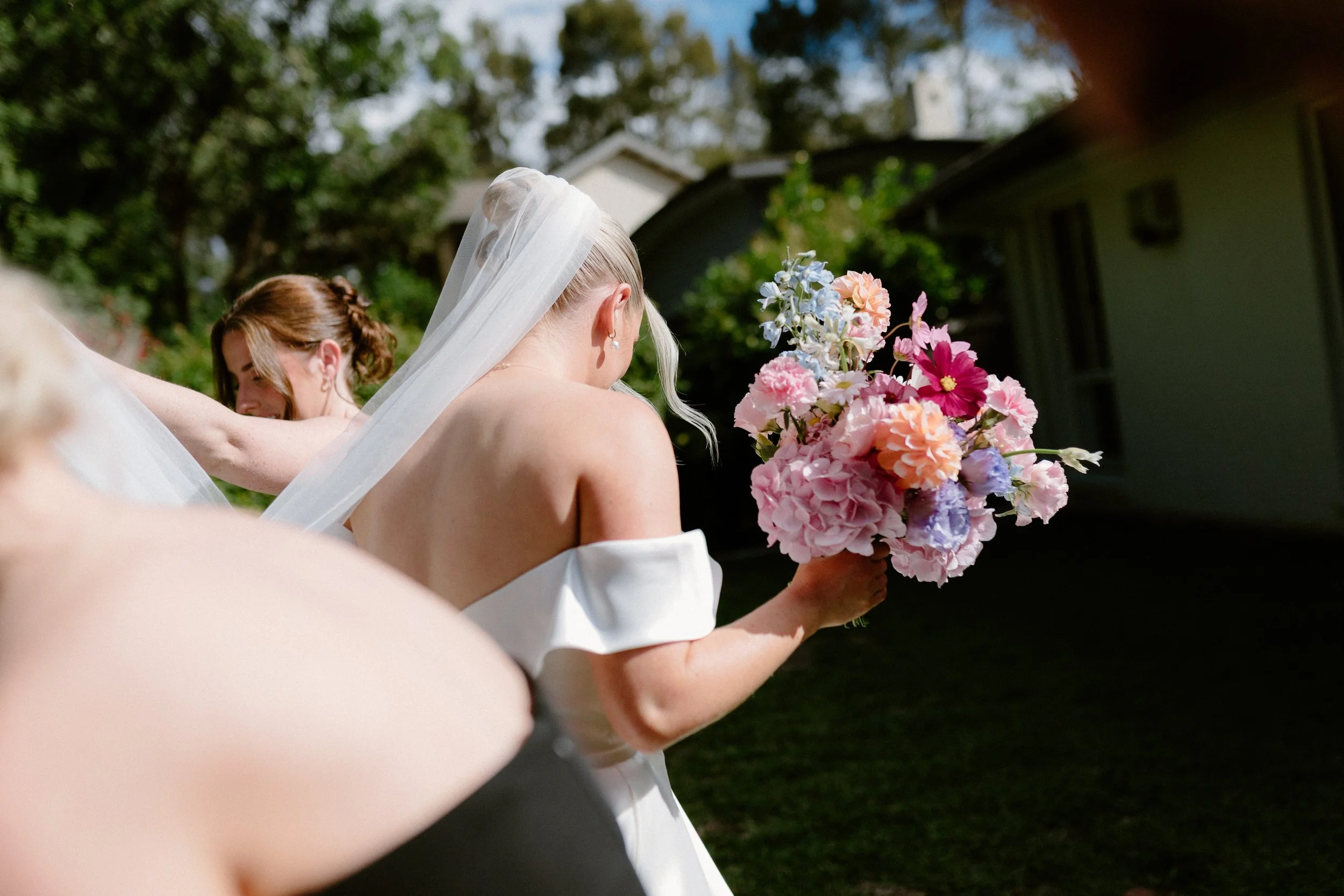 A bride holding a bouquet of pastel pink, blue, and purple flowers outdoors during daytime.