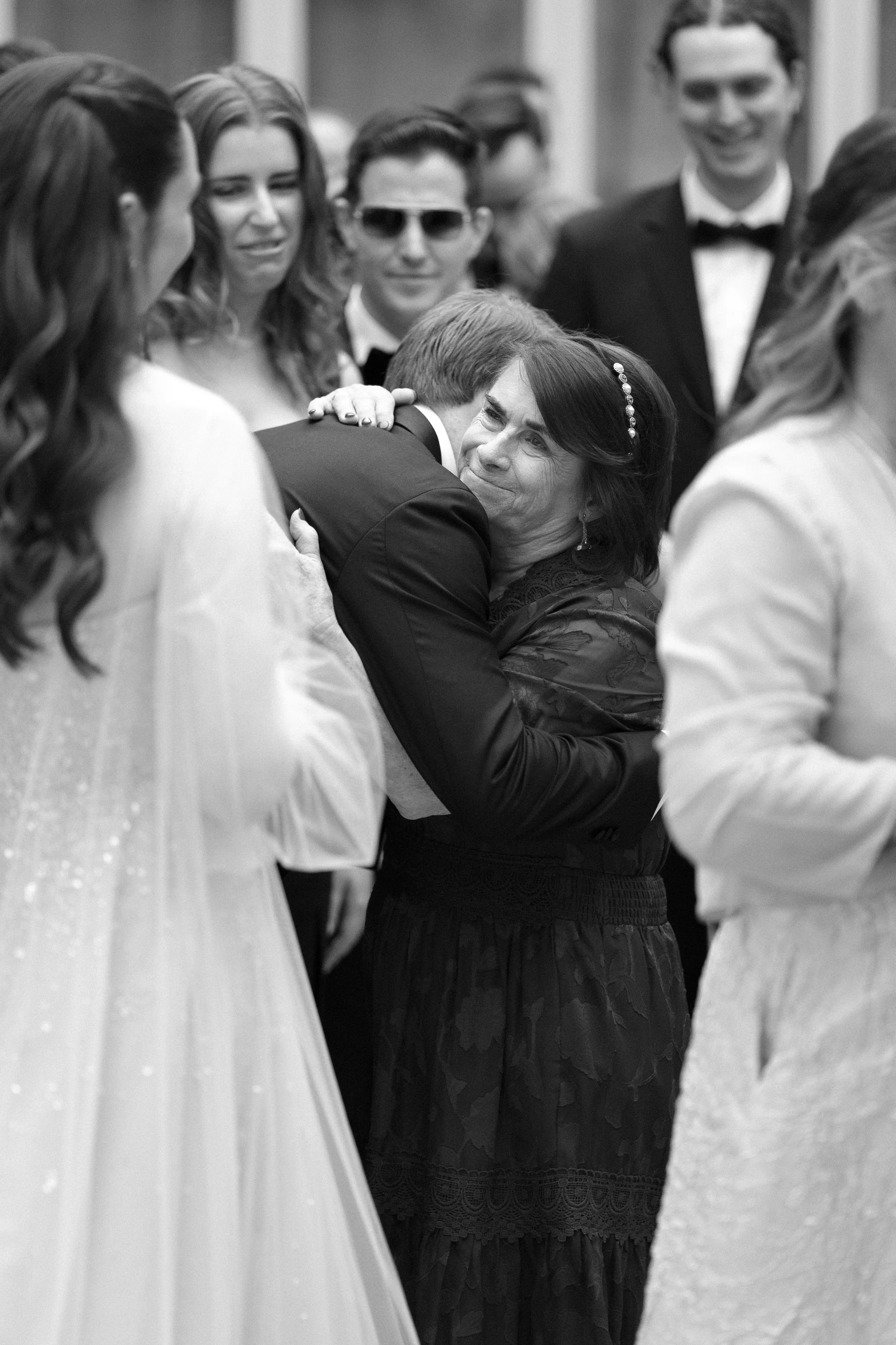 A woman hugging a man at a formal event with several other people in the background.