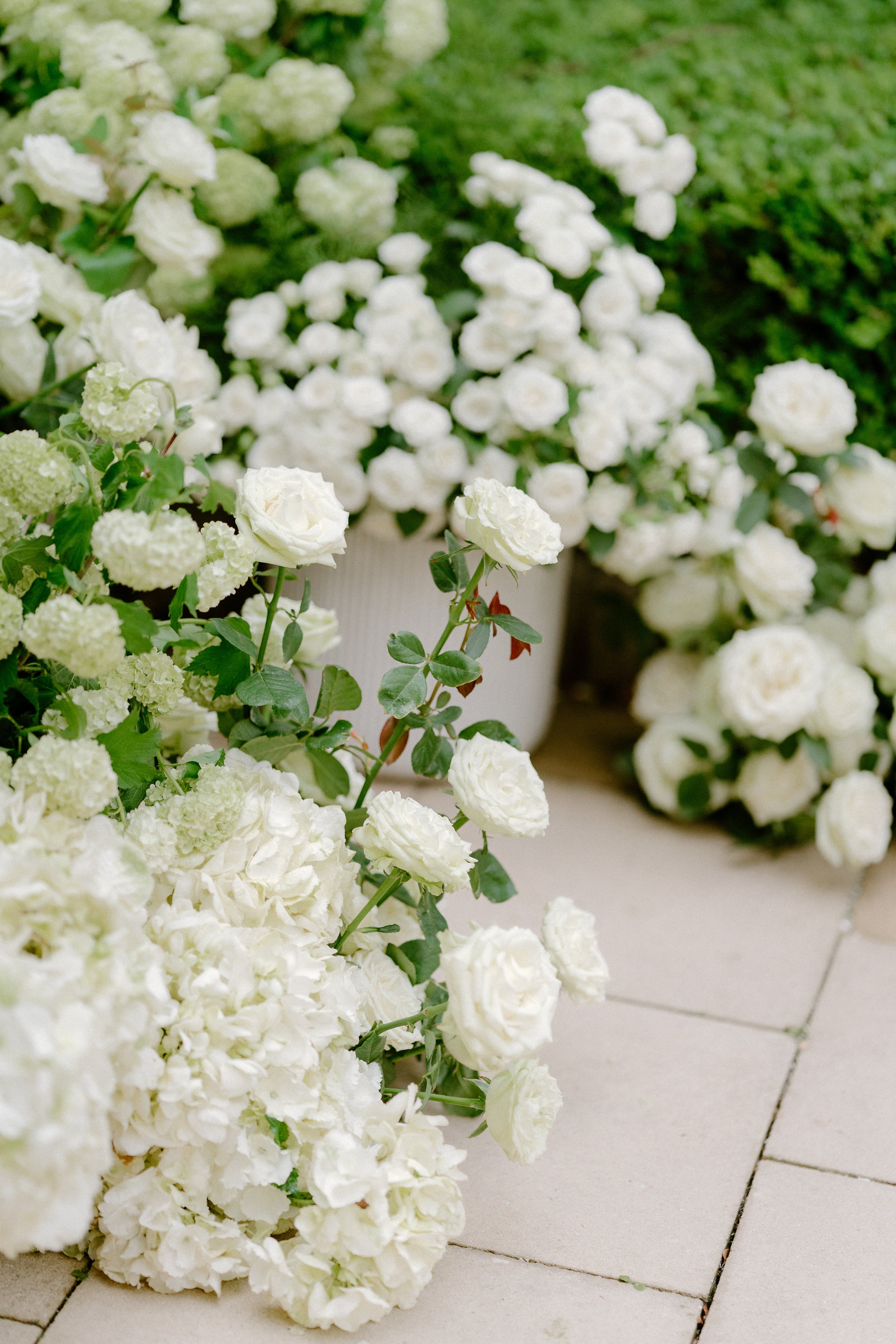 White flowers, including roses and hydrangeas, arranged on a tiled surface outdoors.