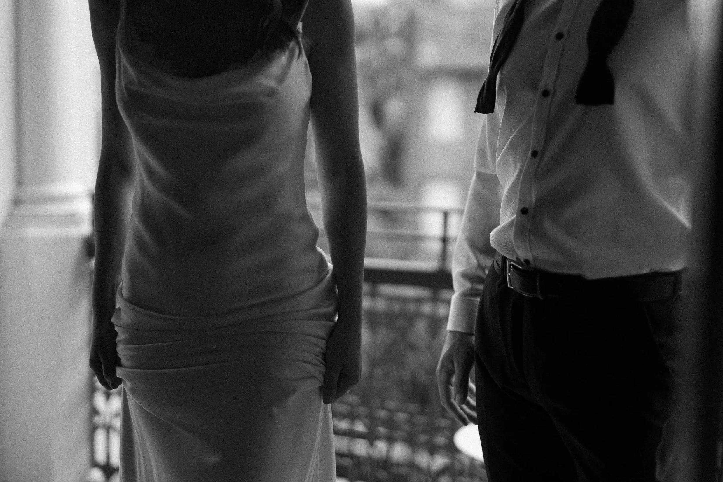 Close-up shot of a man and a woman in formal attire, standing indoors near a balcony or window in black and white.