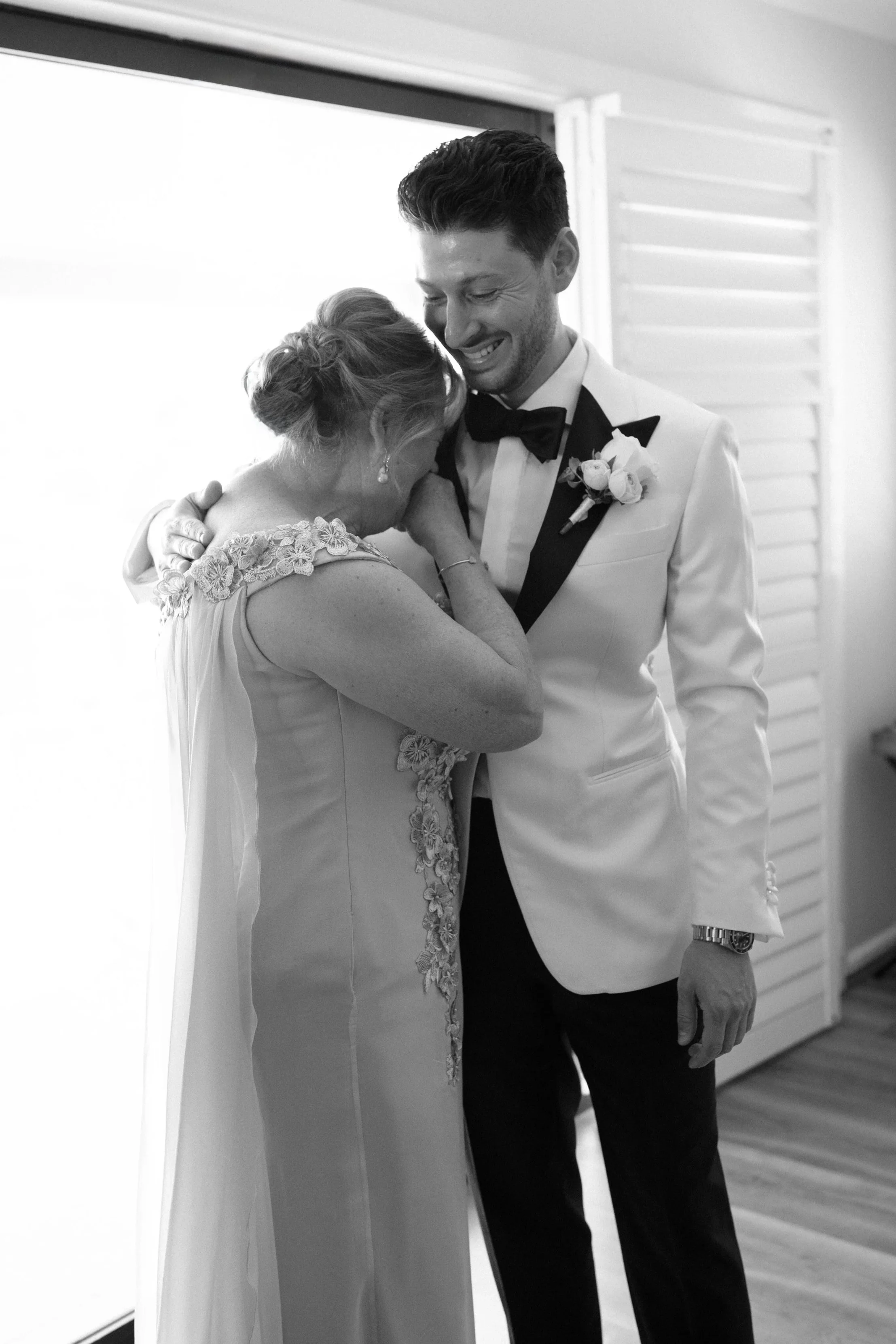 A bride and groom share a tender moment, hugging and crying, in a black-and-white photo on their wedding day.