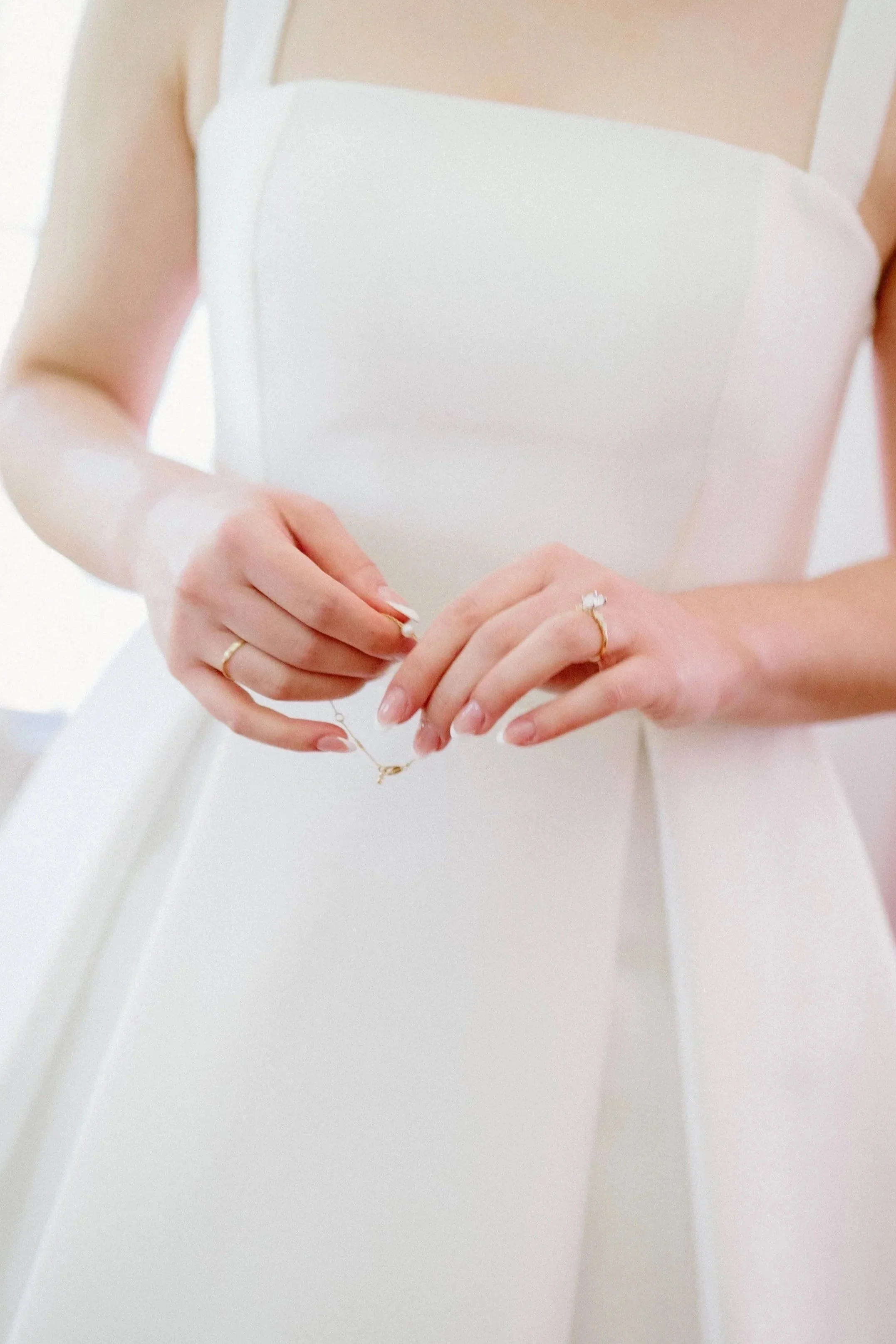 Person in a white dress holding a jewelry piece.