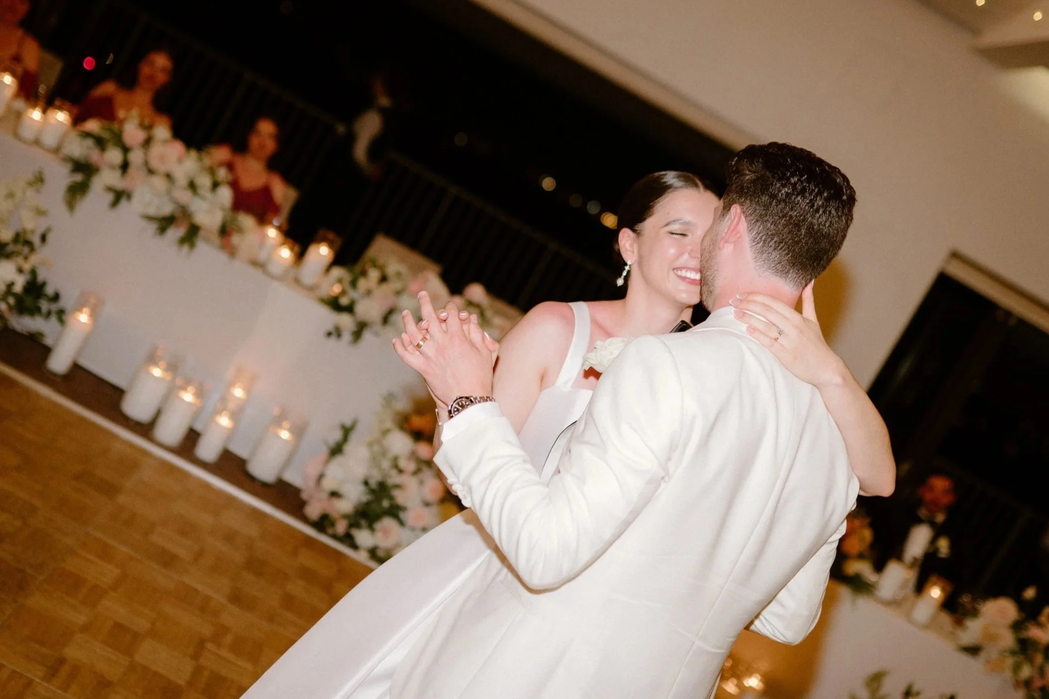 A bride and groom dance together at their wedding reception, smiling and holding each other close.