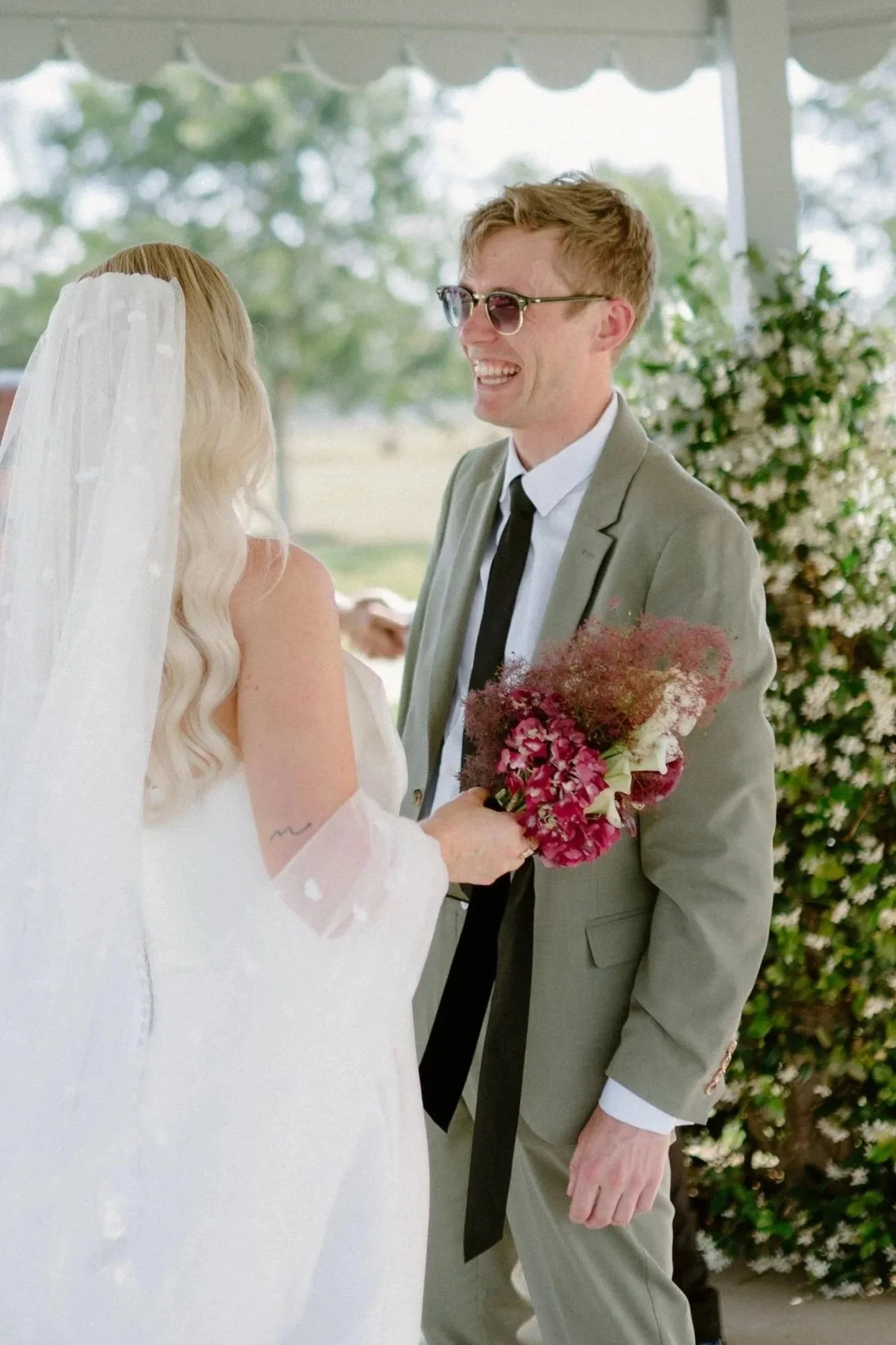 A bride and groom sharing a moment during their outdoor wedding ceremony, with the bride holding a colorful bouquet and both smiling.