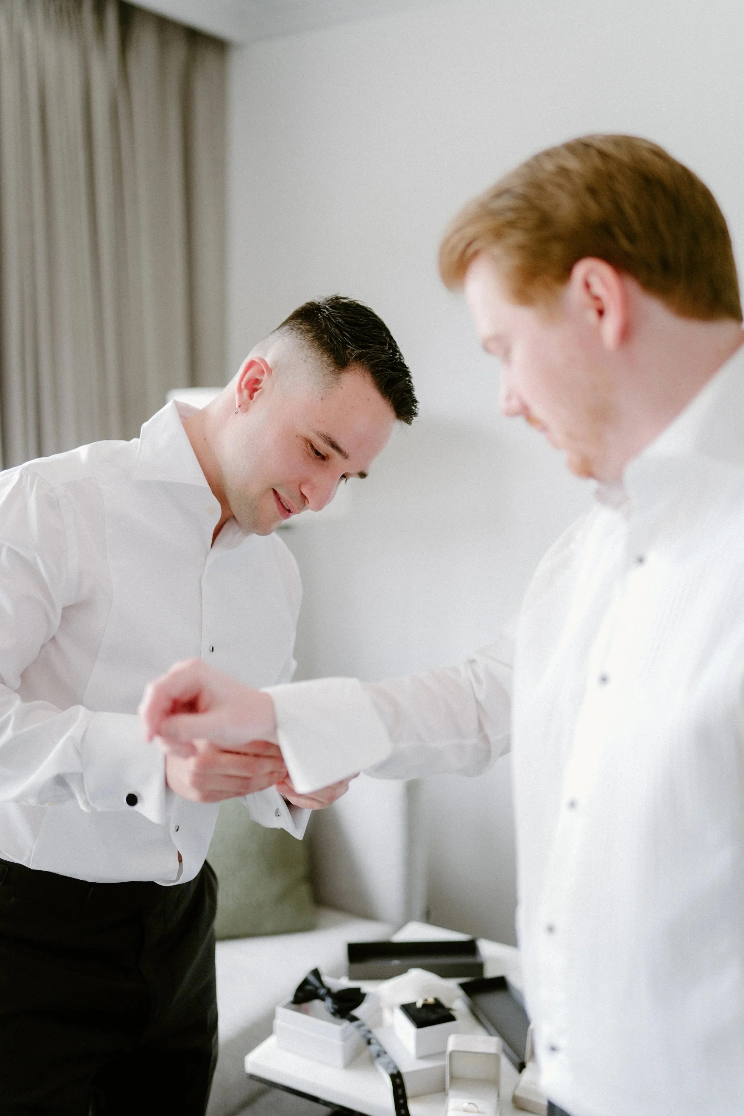 Two men in white dress shirts exchanging a handshake in a room with gift boxes on a table.
