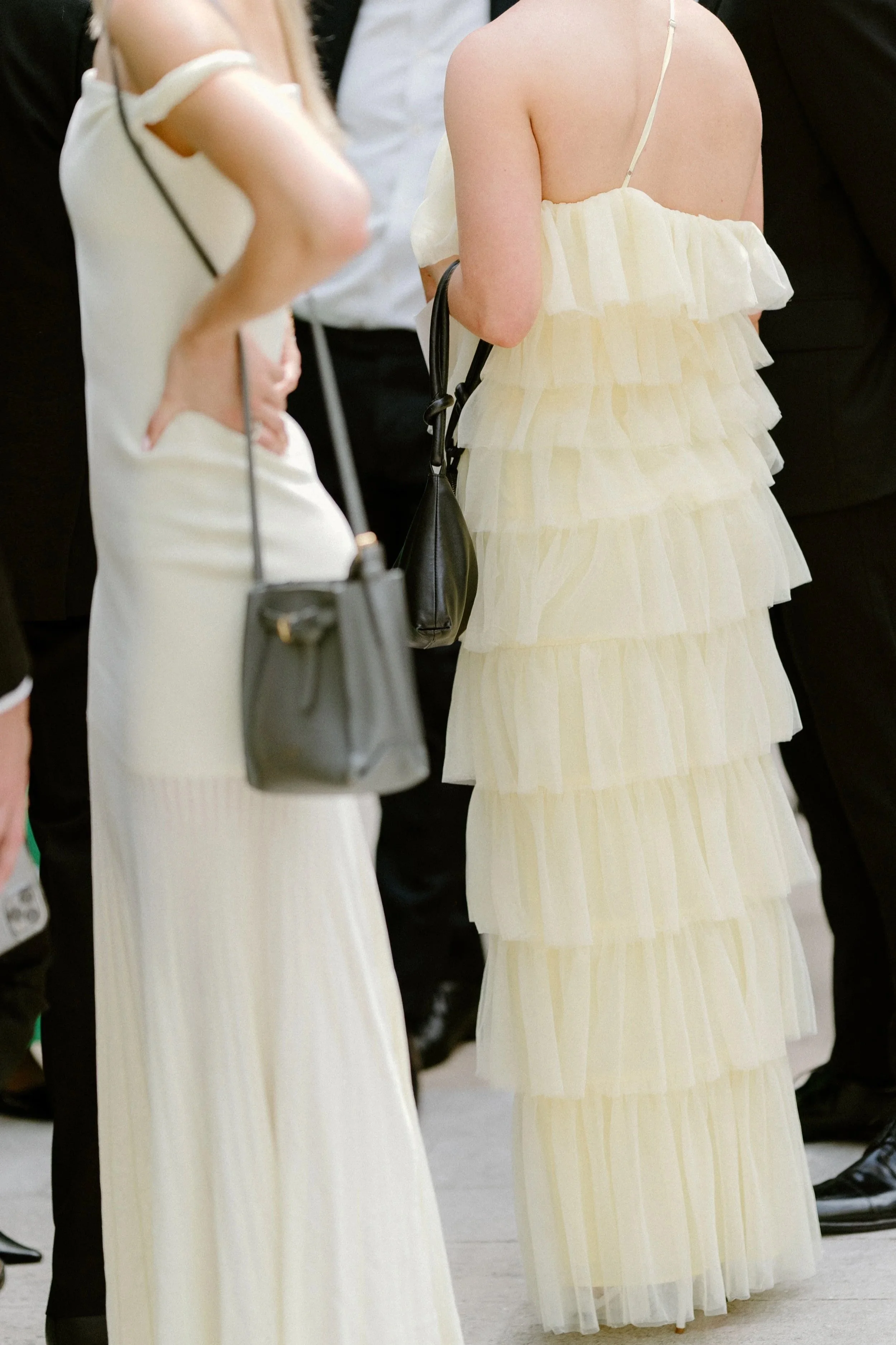 People in elegant dresses and handbags at a formal event or gathering.