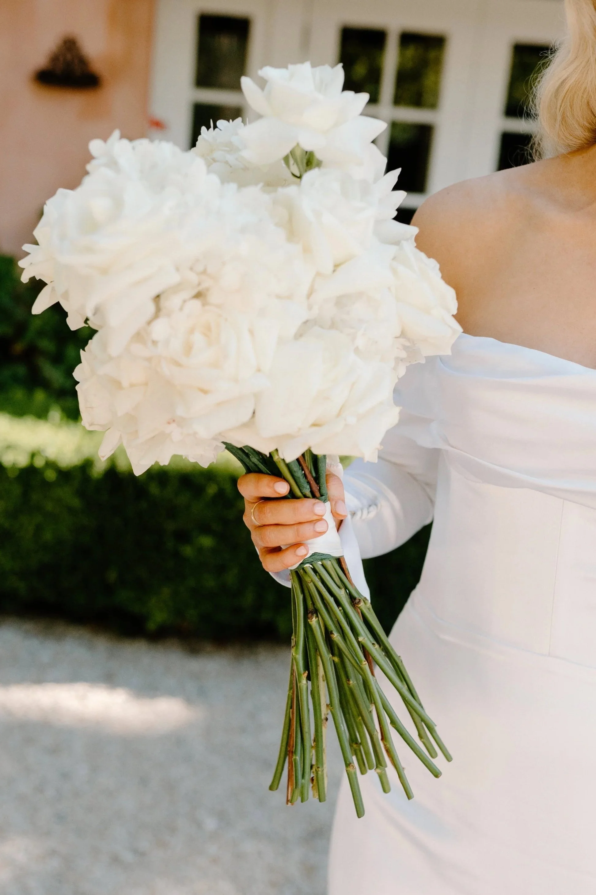 A bride in a white dress holding a large bouquet of white flowers outdoors.