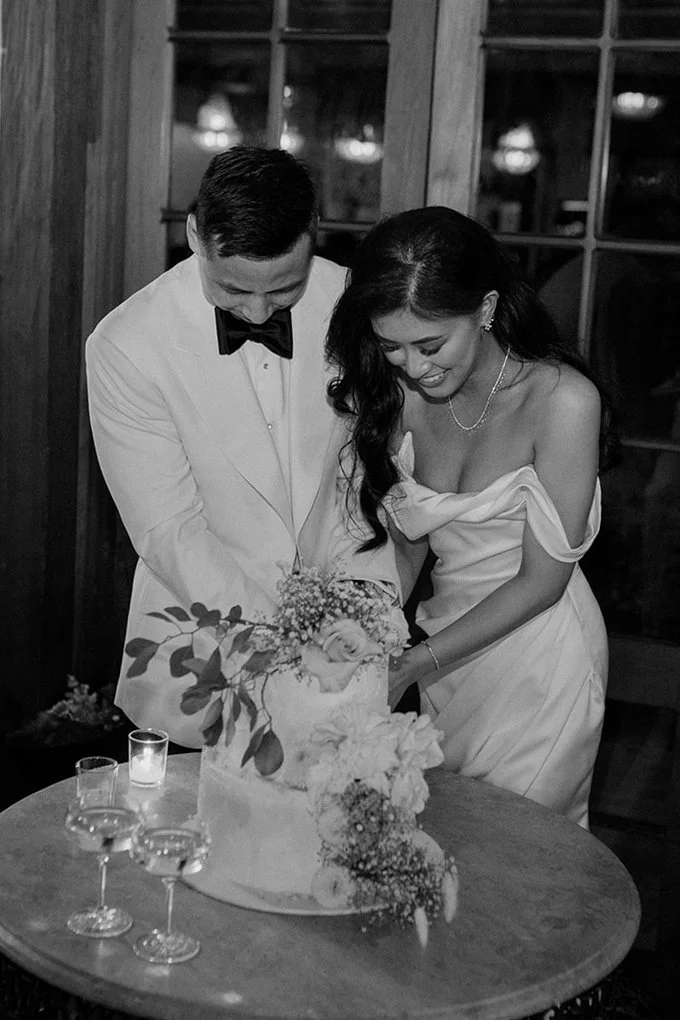 Bride and groom in formal attire cutting a wedding cake.