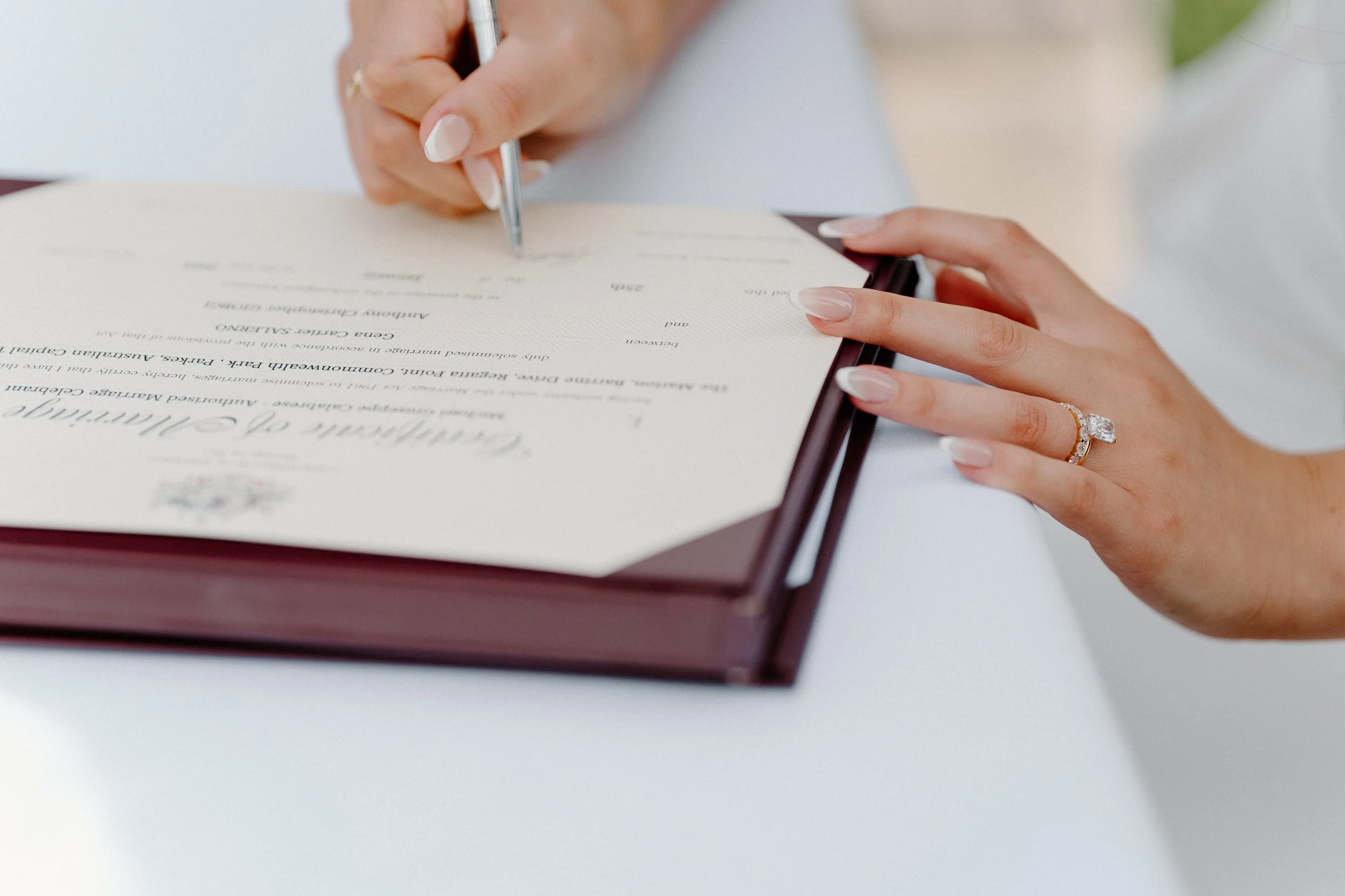 A person signing a marriage certificate or wedding document with a pen, wearing an engagement ring.