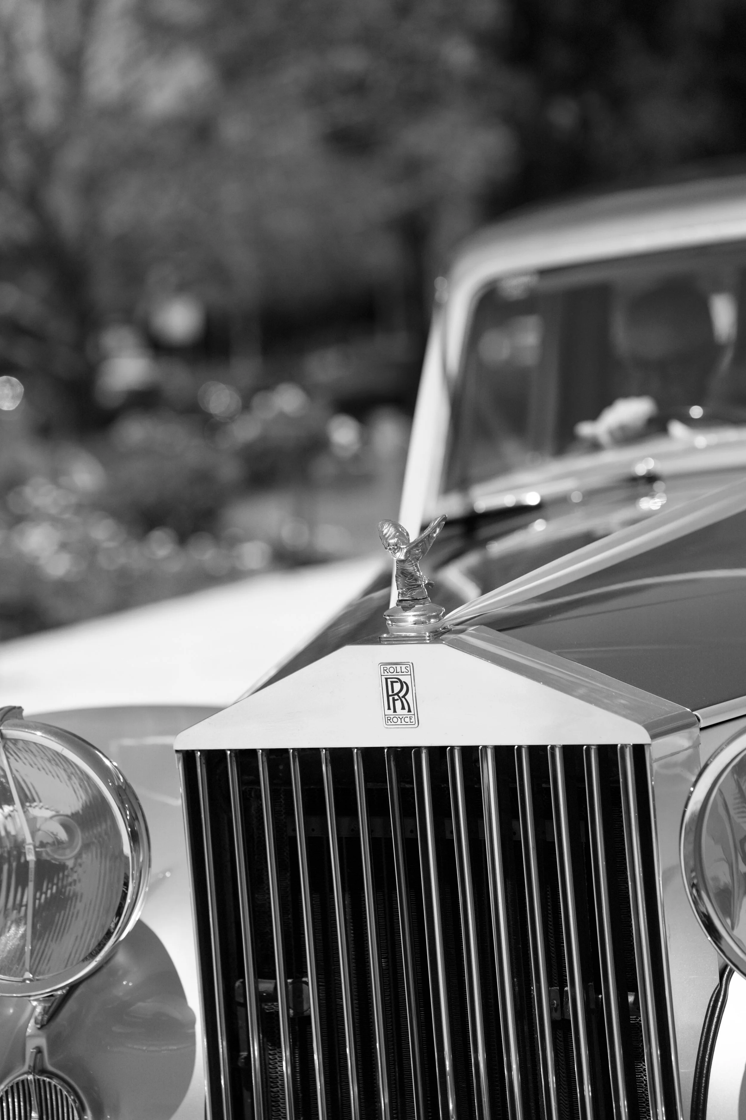 Close-up of a vintage Rolls Royce car hood ornament and front grille in black and white