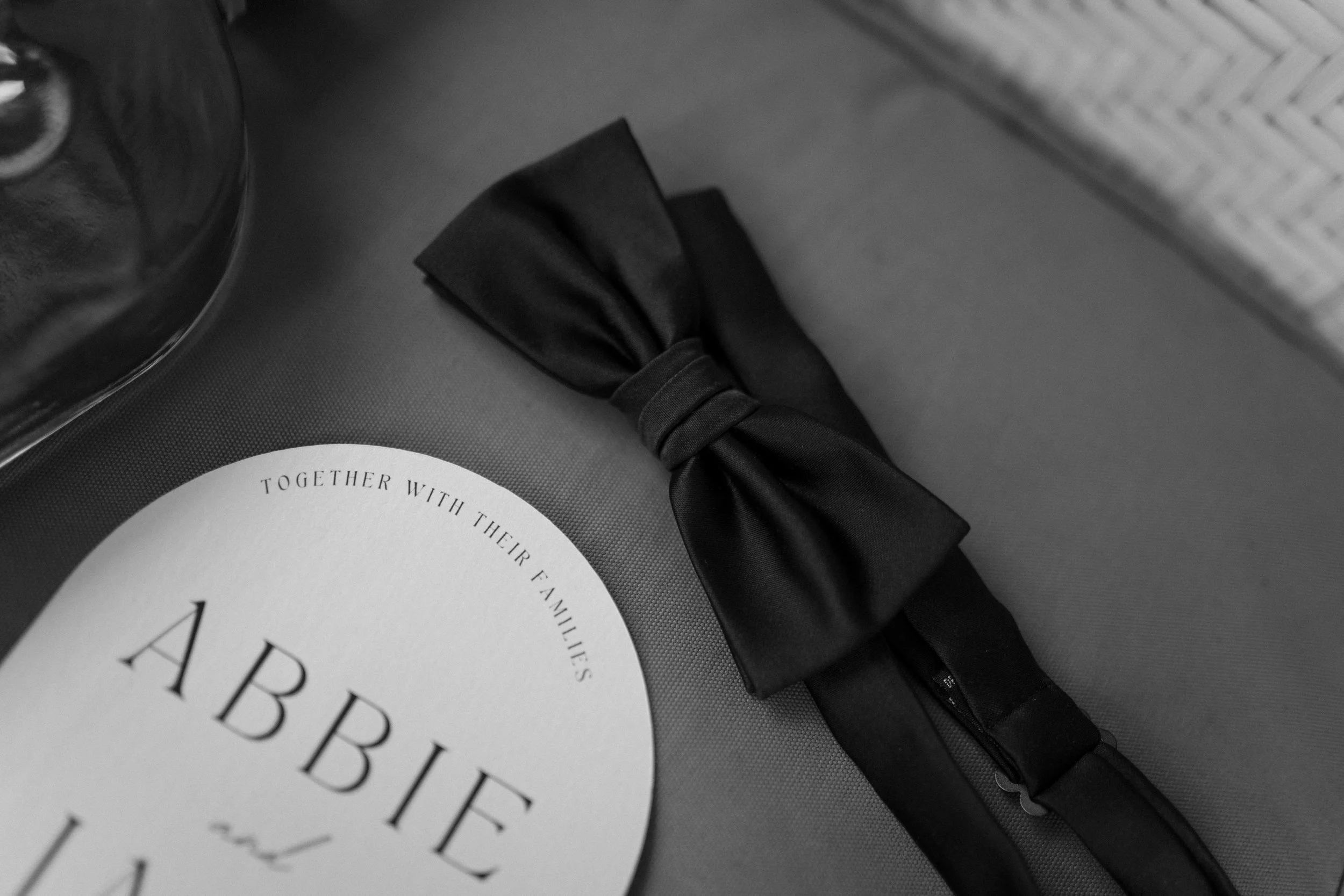 Black gift box with a satin ribbon and a white circular card with black text, partially visible.