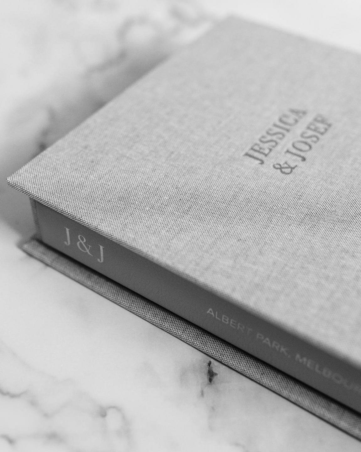 A close-up of a textured, light-colored book cover with the title 'J & J' and a spine that reads 'Albert Park Melbourne'.