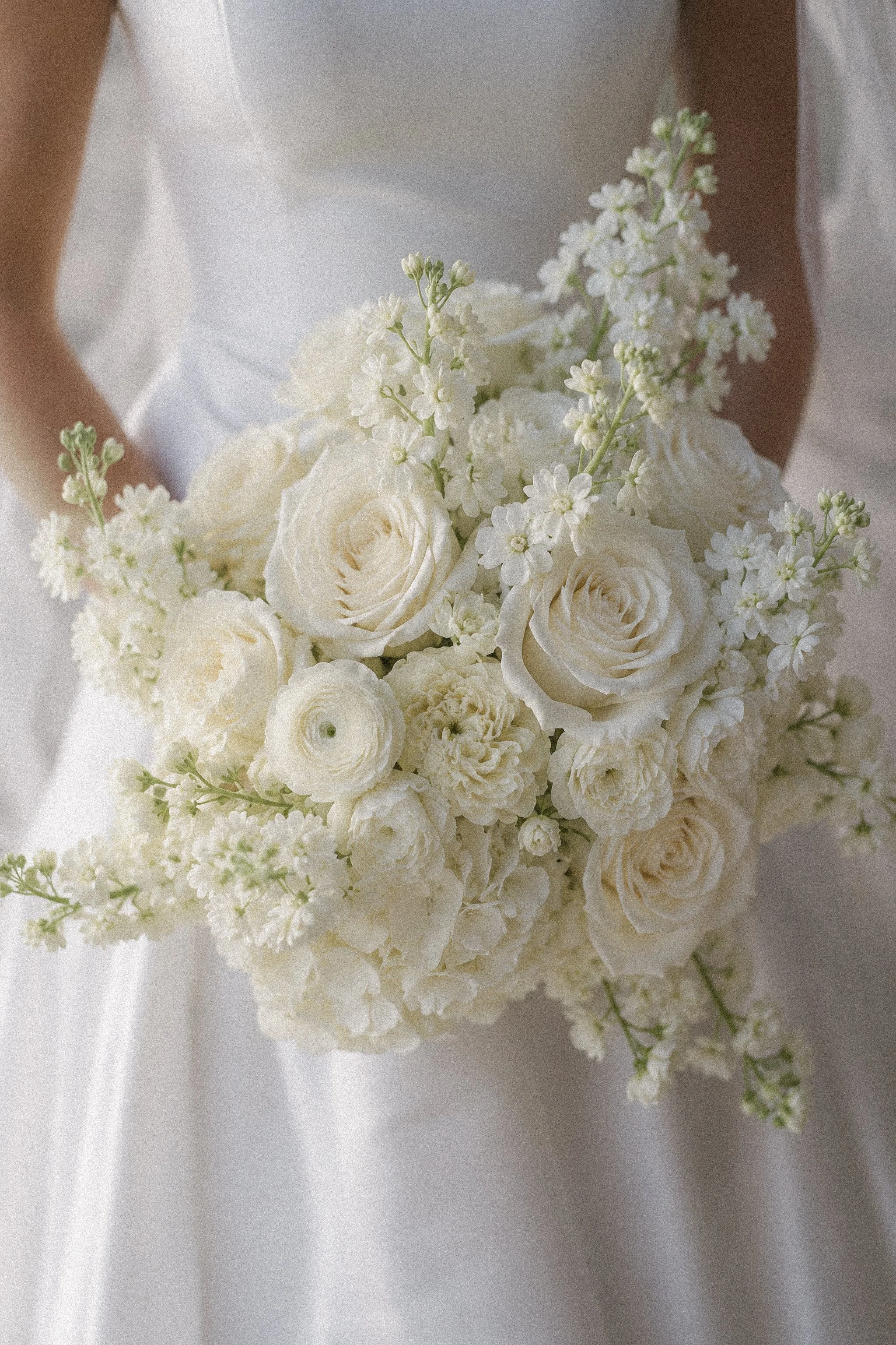 A wedding bouquet with white roses and small white flowers resting on white fabric.