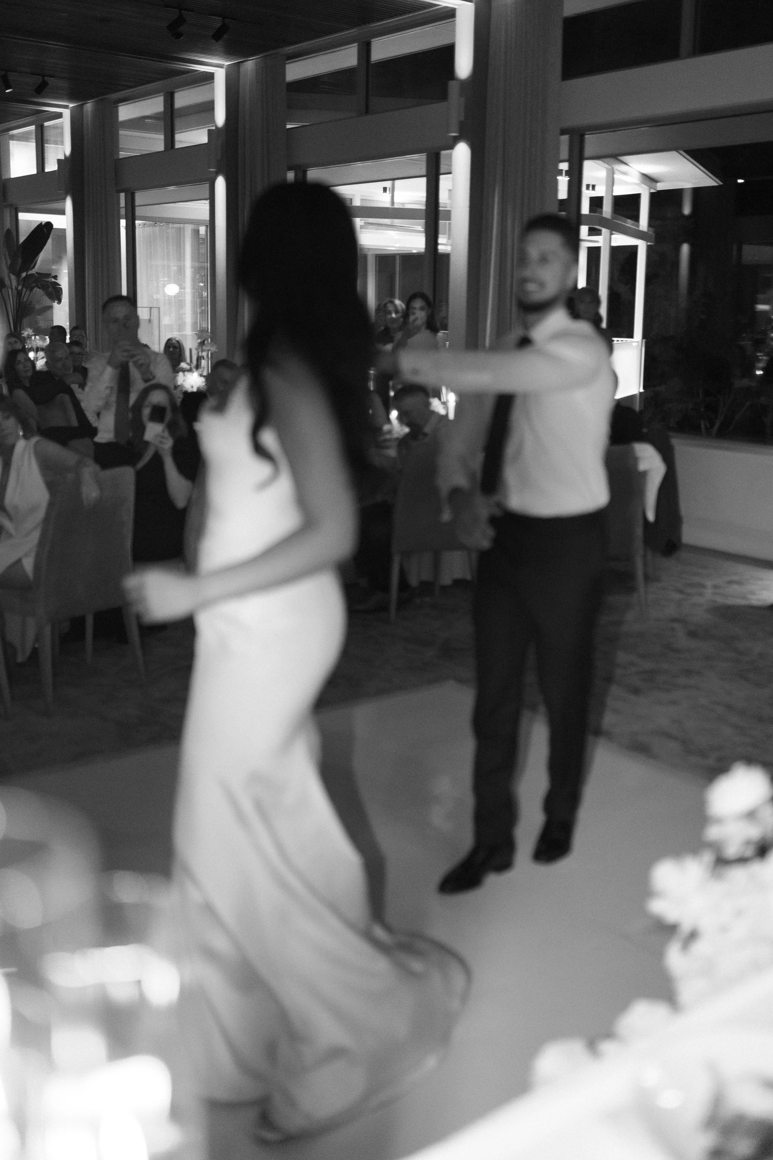 Couple dancing at a wedding reception with seated guests in the background.
