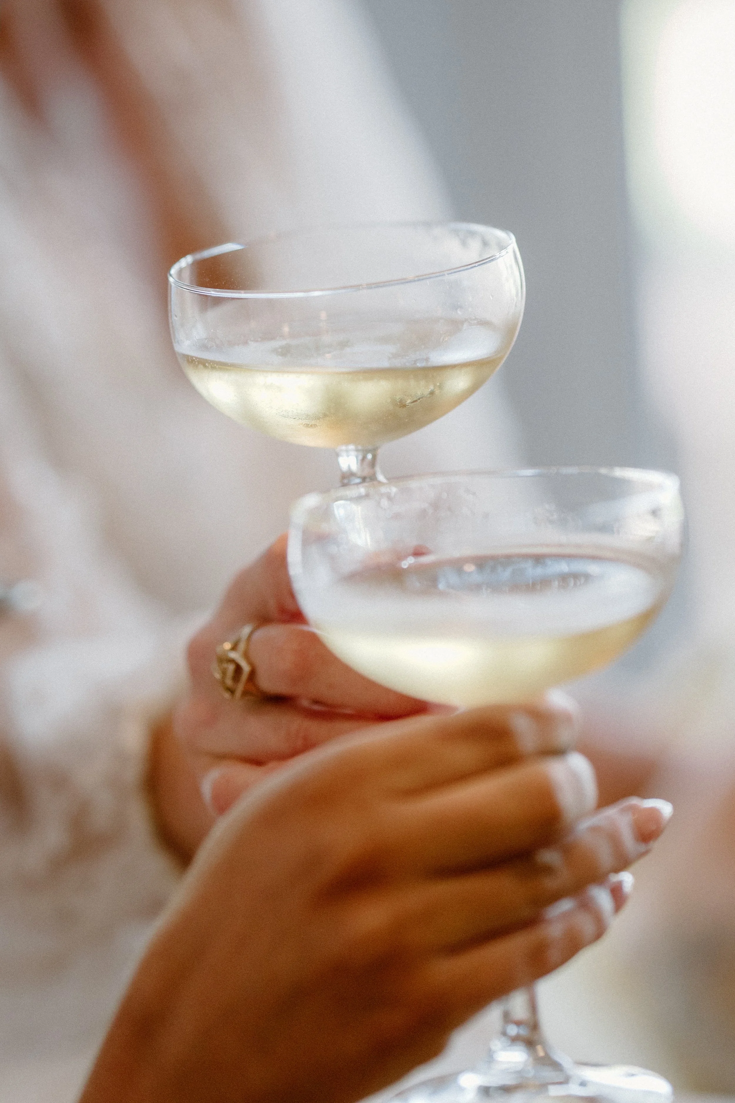 Close-up of a person holding two coupe glasses filled with white wine.