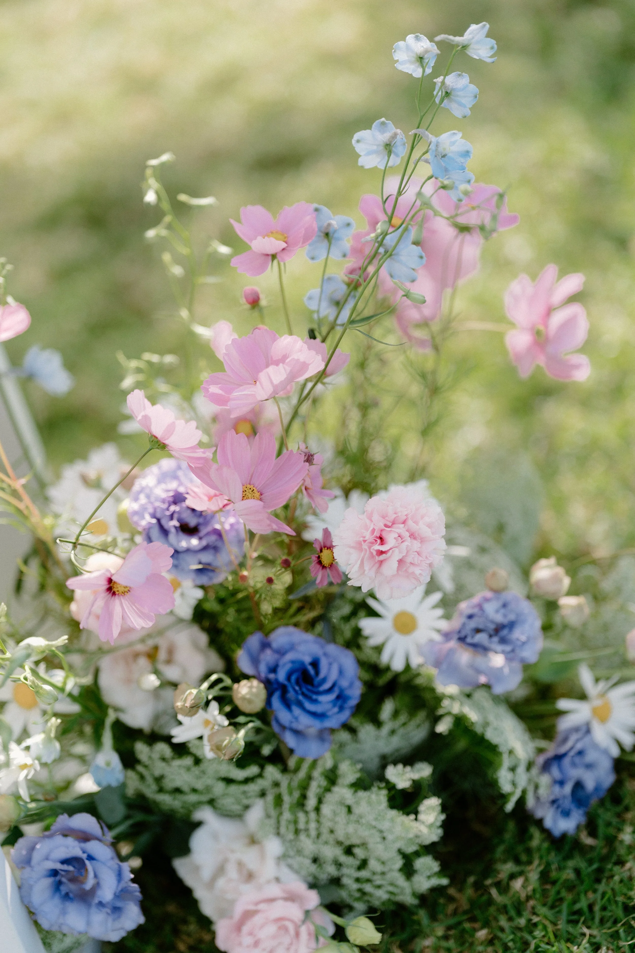 A colorful flower arrangement with pink, blue, and white flowers on a grassy background.