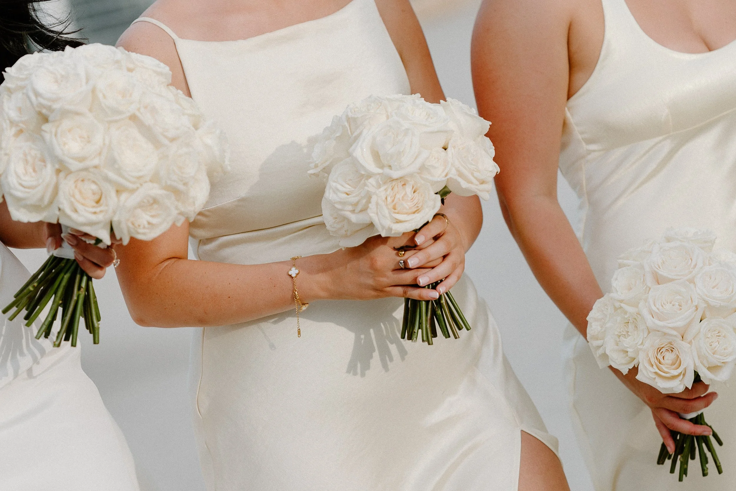 Women in white dresses holding white rose bouquets at a wedding.