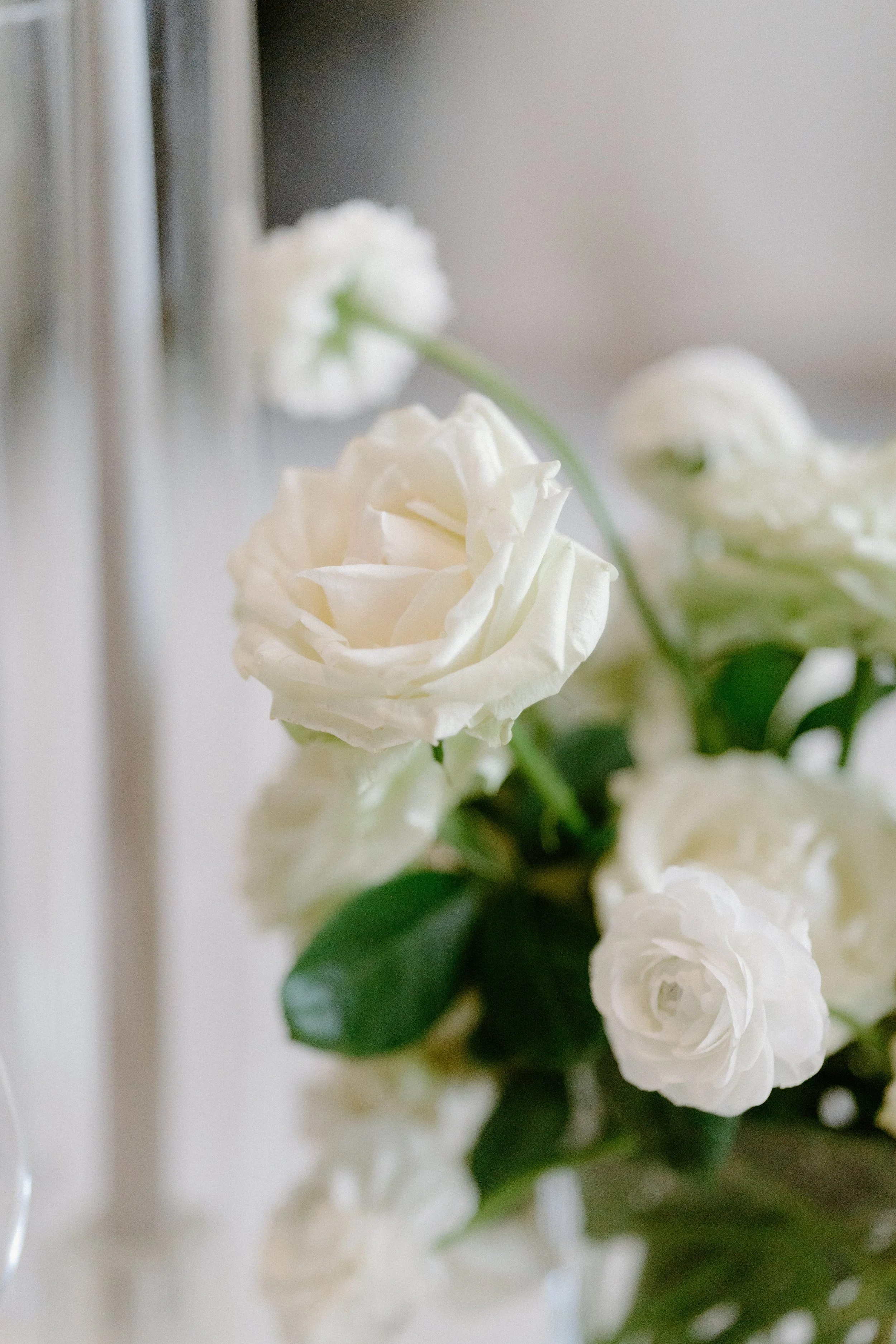 Close-up of a white roses bouquet with green leaves, placed near a silver candle holder.