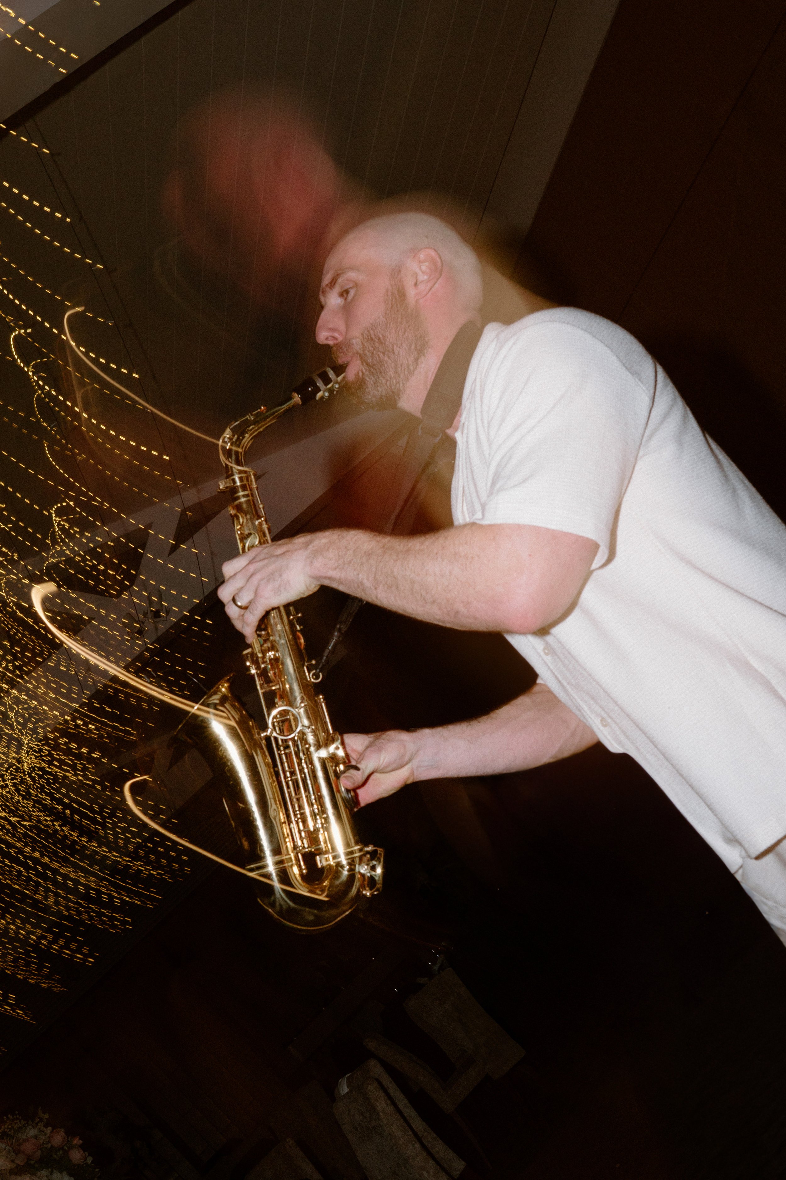 A man playing a saxophone in a dimly lit room with abstract light trails.