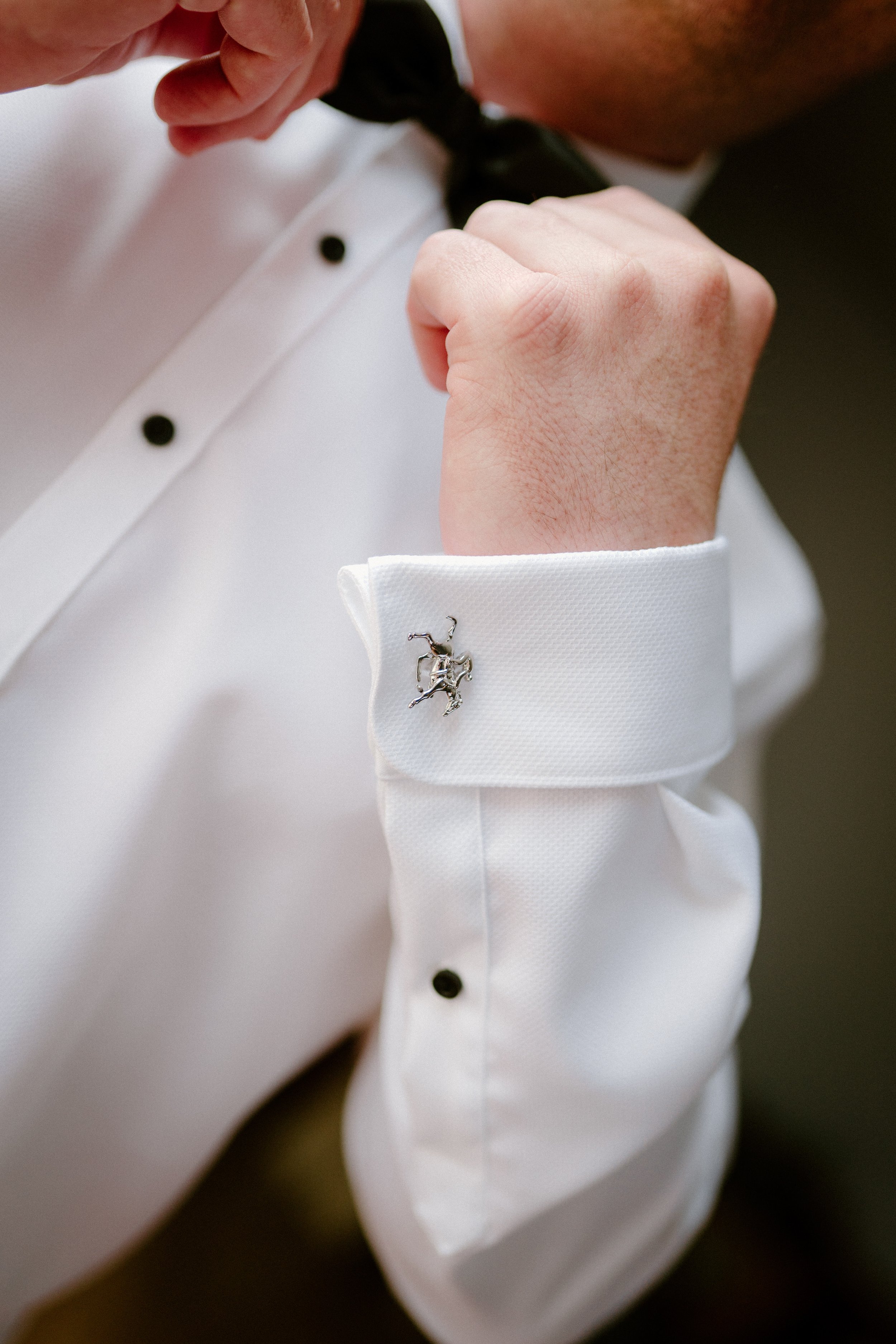 The Sienna, Hunter Valley Wedding Venue, Wedding Photos. Close-up of a man adjusting his black bow tie, wearing a white dress shirt with French cuffs, which has a silver cufflink shaped like a horse.
