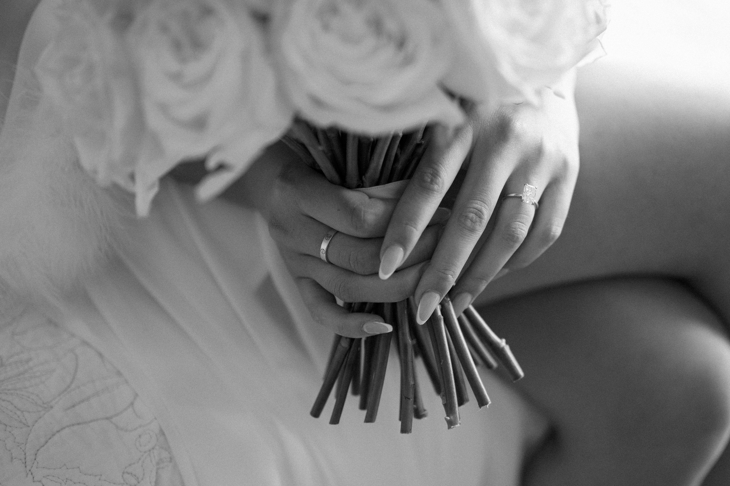 Close-up of a woman's hands holding a bouquet of flowers, with a visible wedding ring on her finger, in black and white.