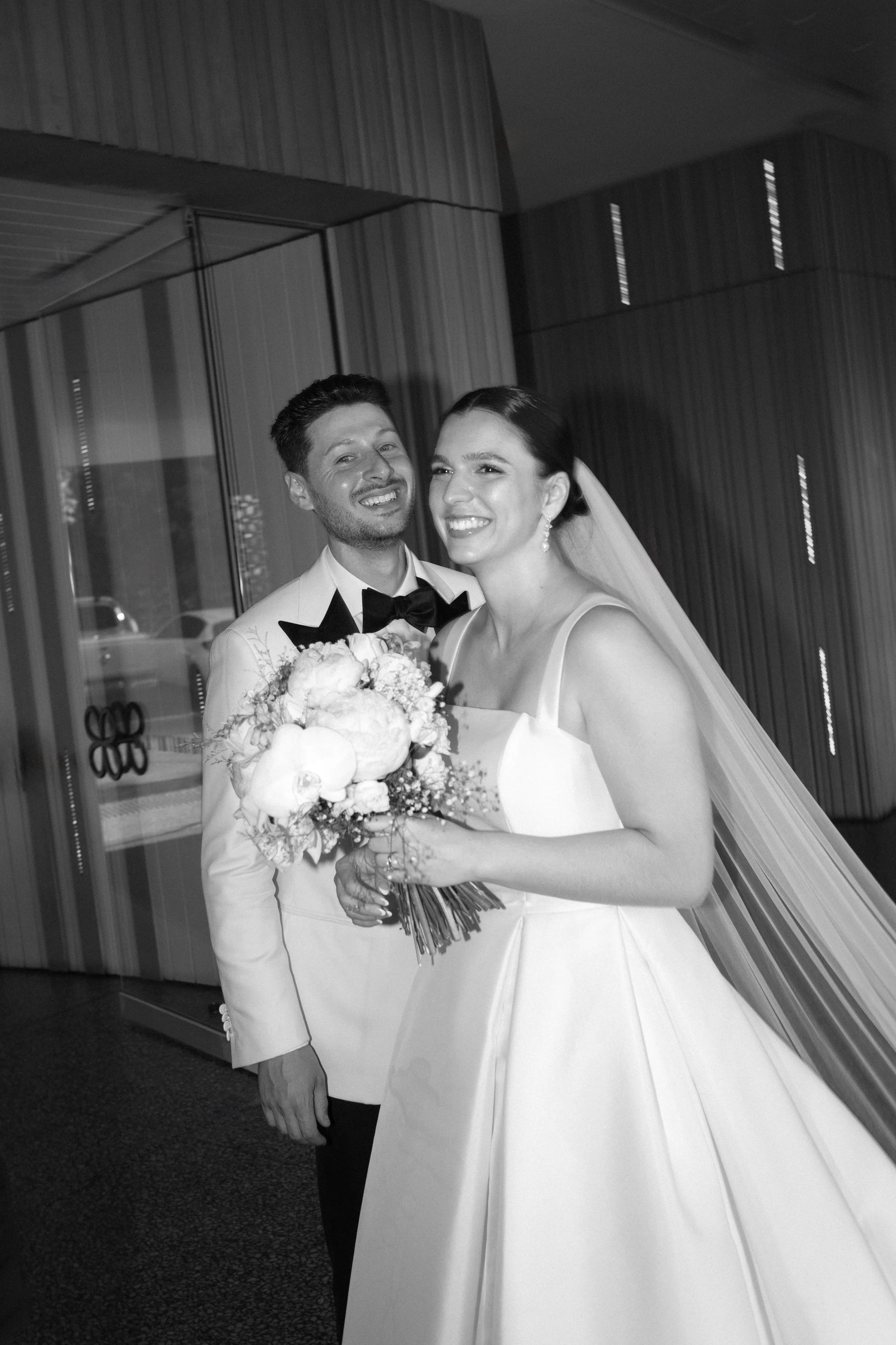 Sergeants Mess, Mosman Wedding Venue. Sergeants Mess Wedding Photos. Black and white photo of a bride and groom on their wedding day, smiling and posing together, with the bride holding a bouquet of flowers.