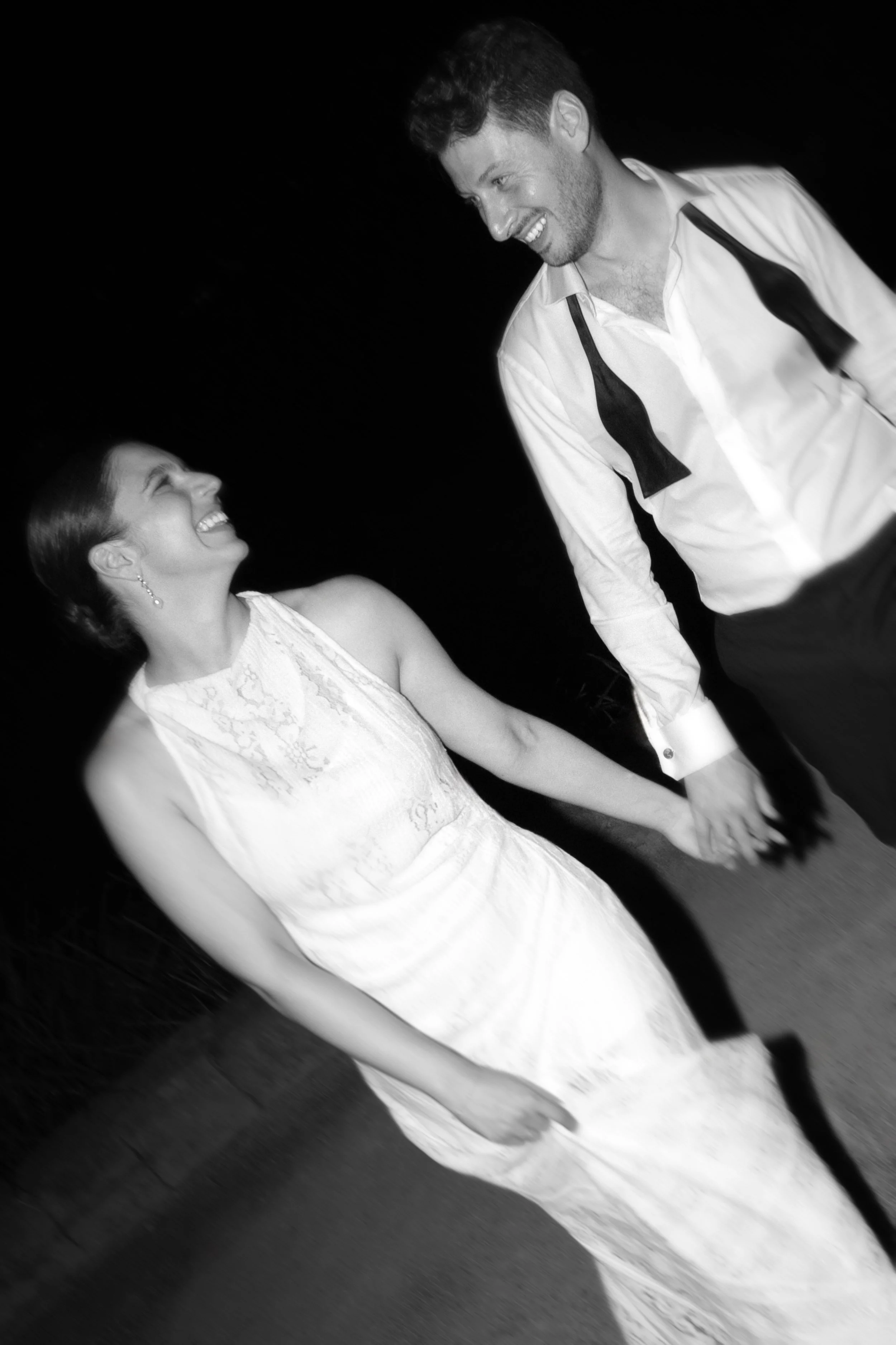 A woman and a man in formal attire holding hands and smiling at each other at night.