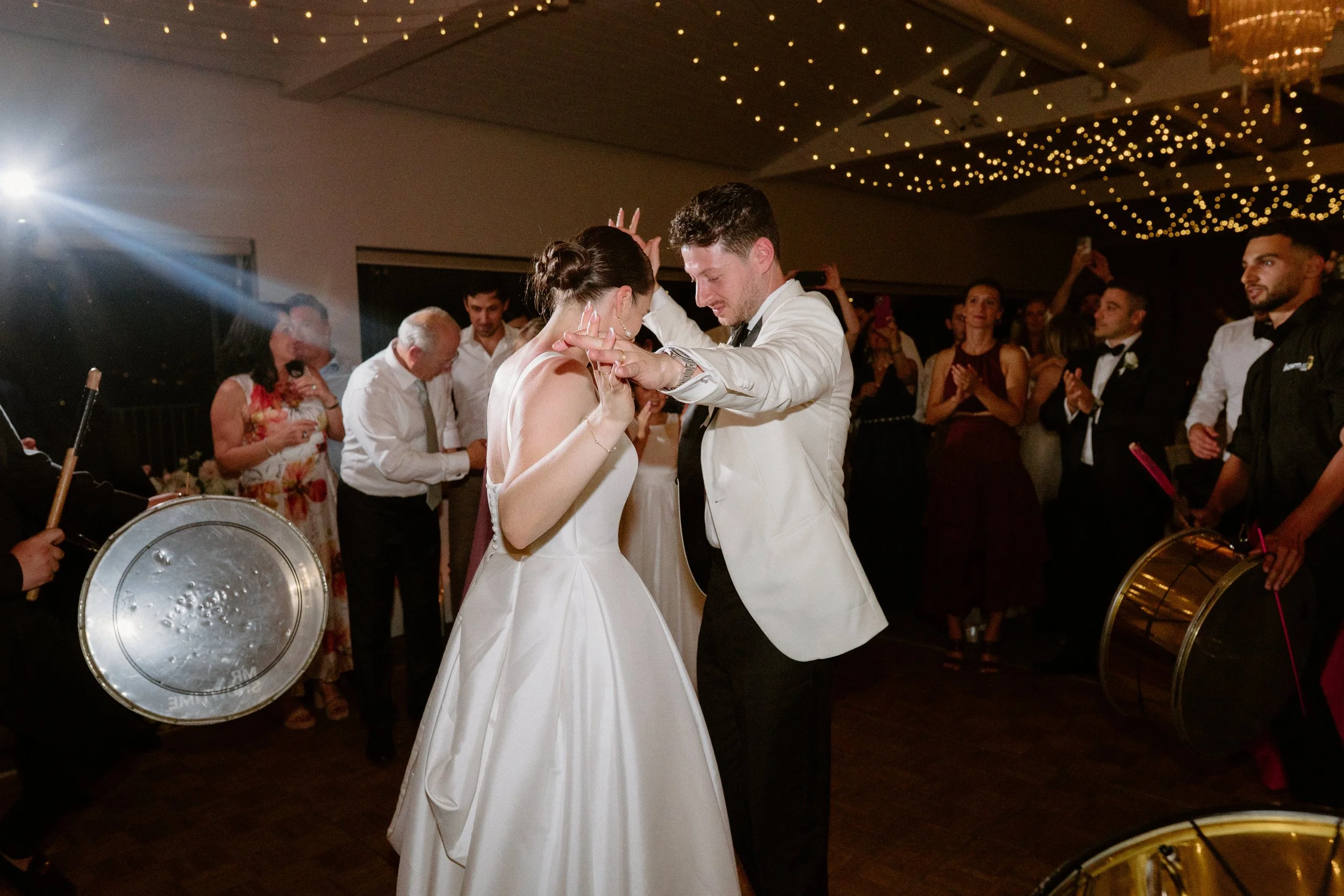 Sergeants Mess, Mosman Wedding Venue. Sergeants Mess Wedding Photos. A bride and groom dancing at their wedding reception with guests clapping and celebrating around them, and musicians playing drums nearby.