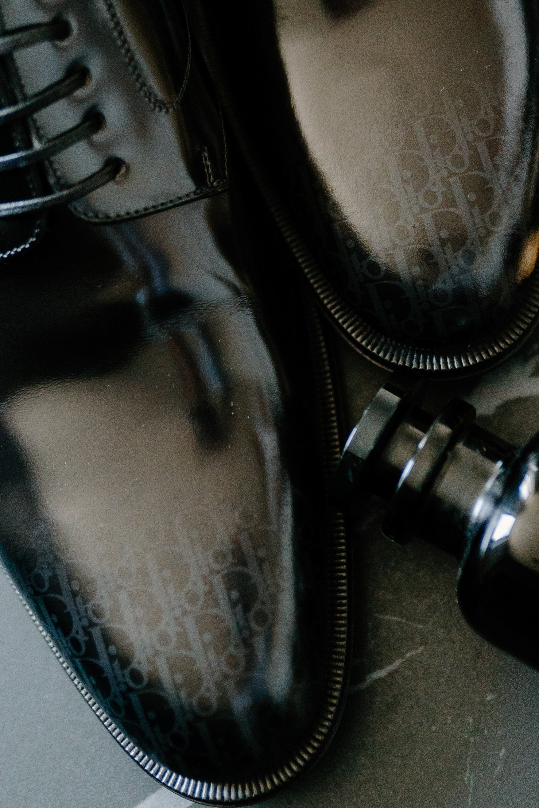 Close-up of black designer shoes with zipper detail and reflective surface, placed on a dark surface.