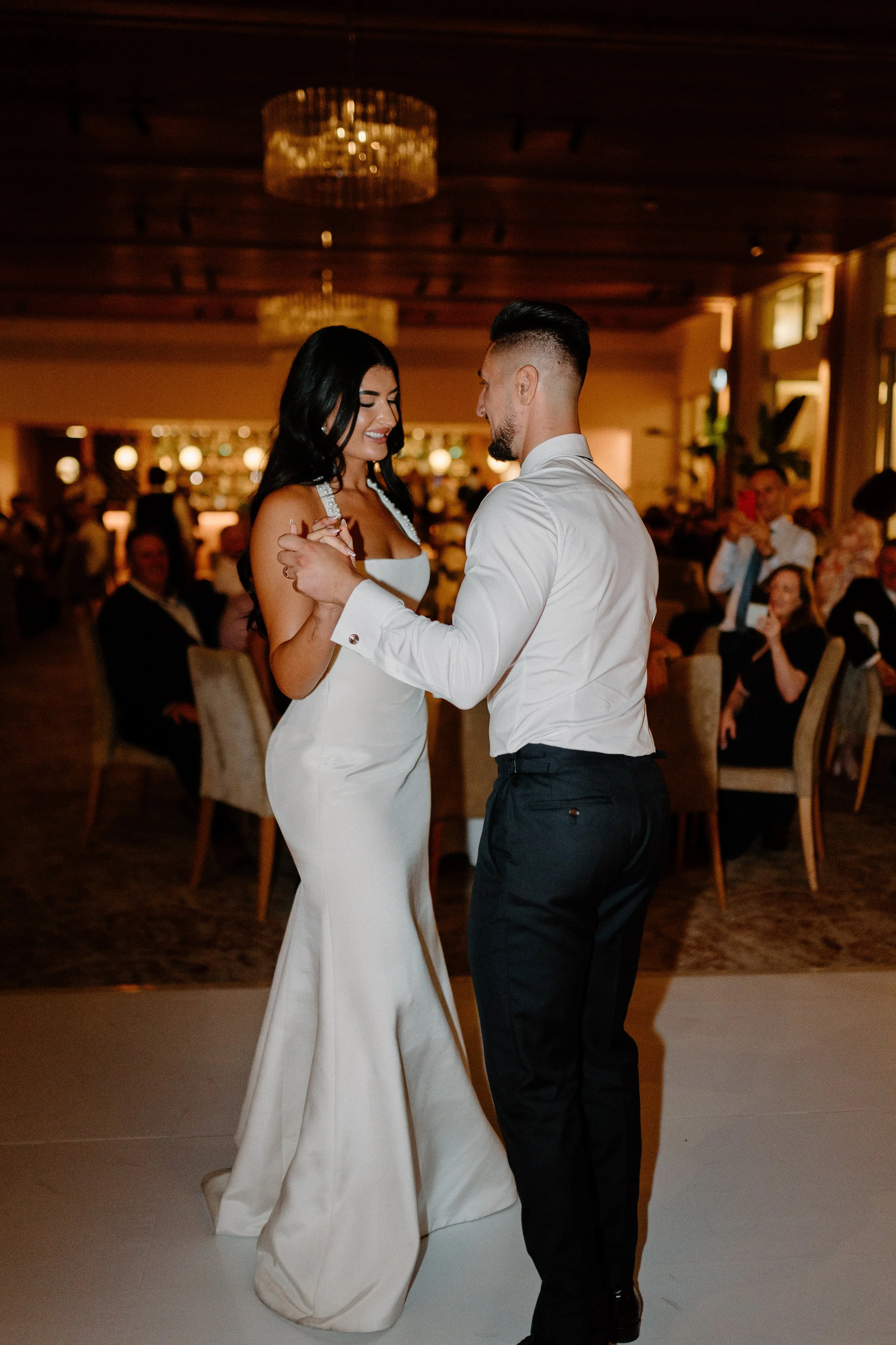 A bride and groom share their first dance at their wedding reception, with guests seated around them.