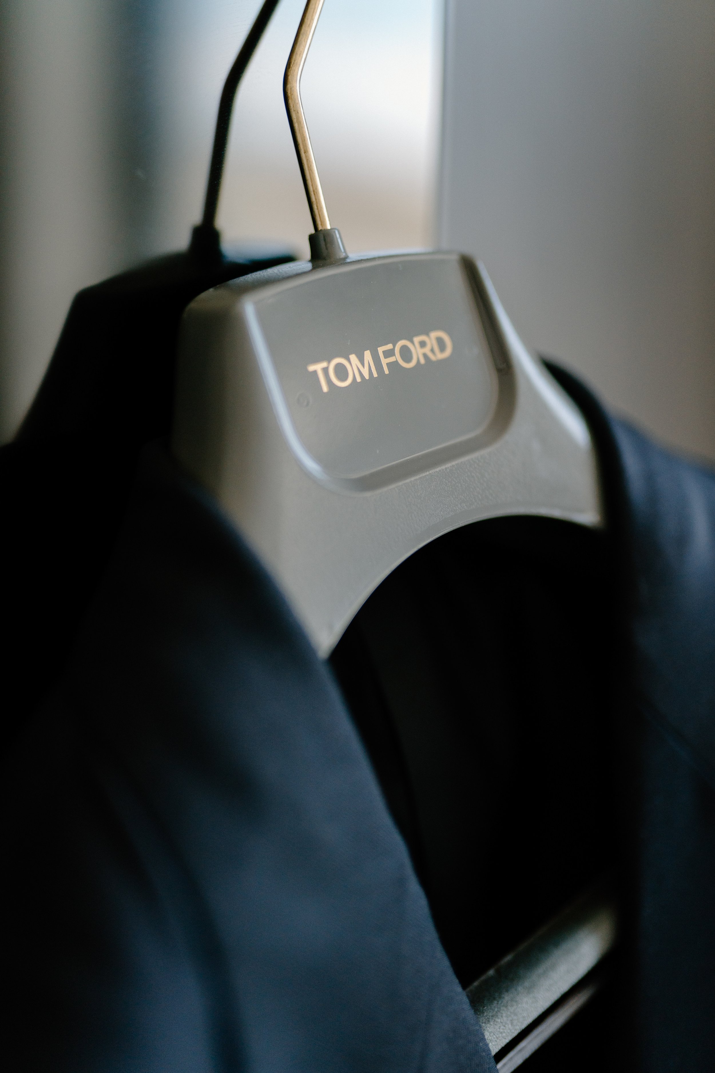 Close-up of a hanger with a gray label reading 'TOM FORD' holding a dark piece of clothing.