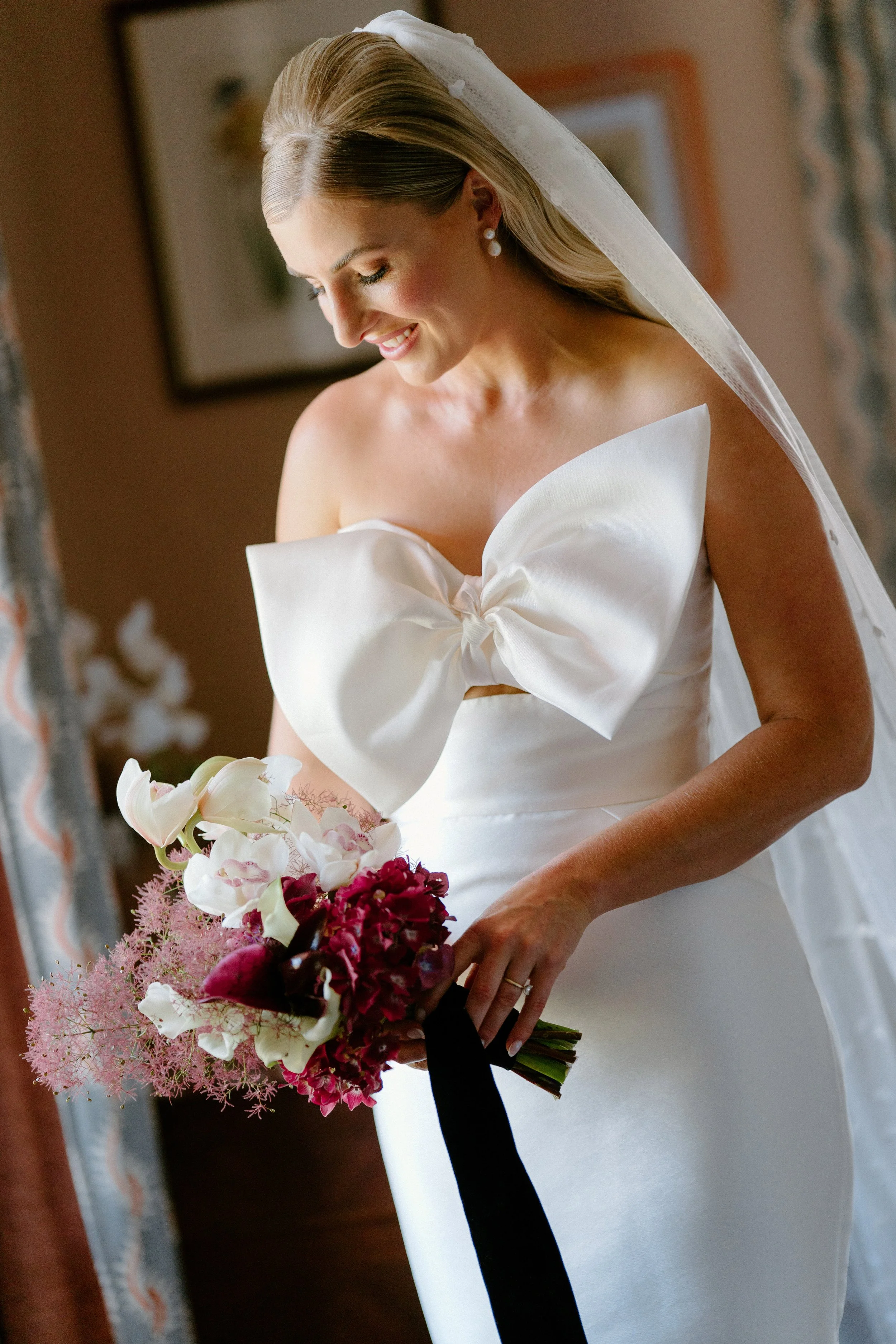 The Sienna, Hunter Valley Wedding Venue, Wedding Photos. Bride in wedding dress holding a bouquet of white orchids, pink flowers, and red blooms, smiling and looking down.