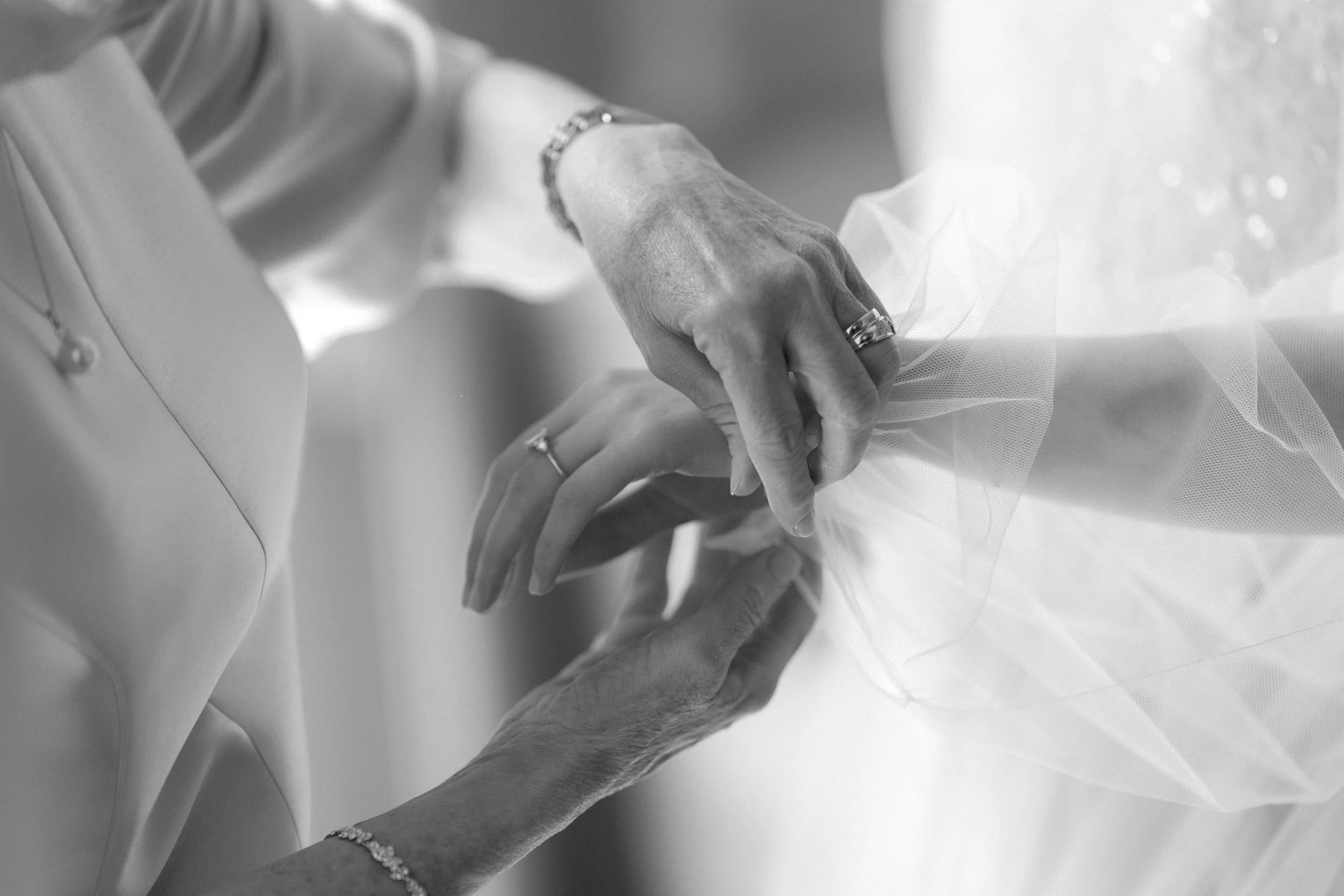 Close-up of two elderly people's hands gently holding each other, with one person wearing a wedding ring, in black and white.