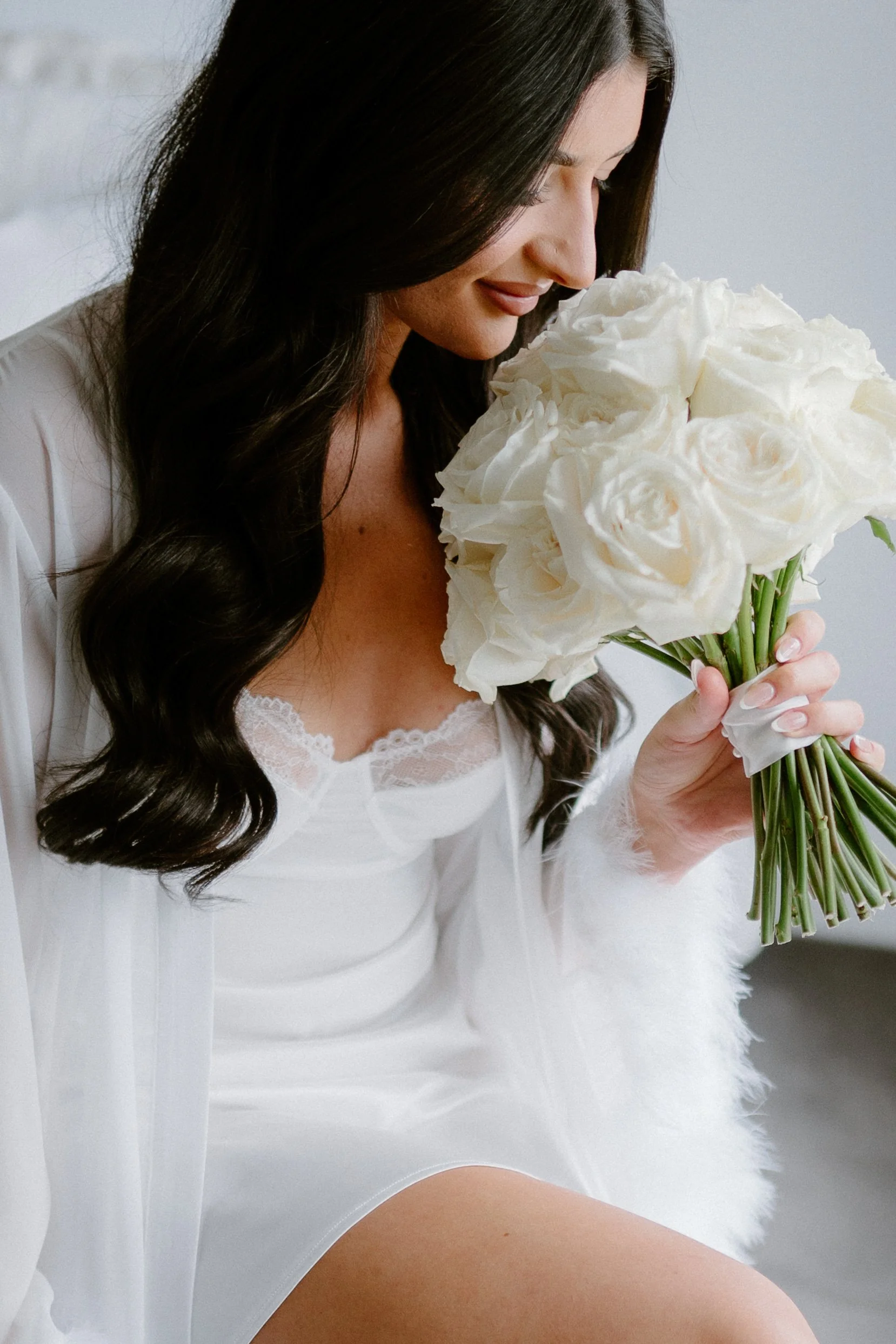 A woman with long dark hair and a lace-trimmed white nightgown holding a bouquet of white roses.