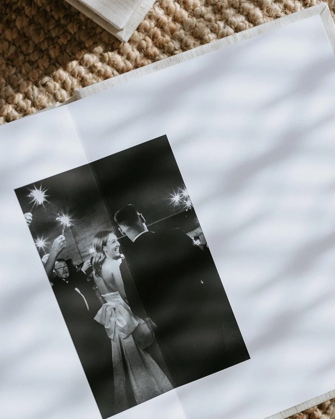 Black and white photograph of a woman in a strapless gown with a large bow in an elegant event, surrounded by people, some holding sparklers, under bright lights.