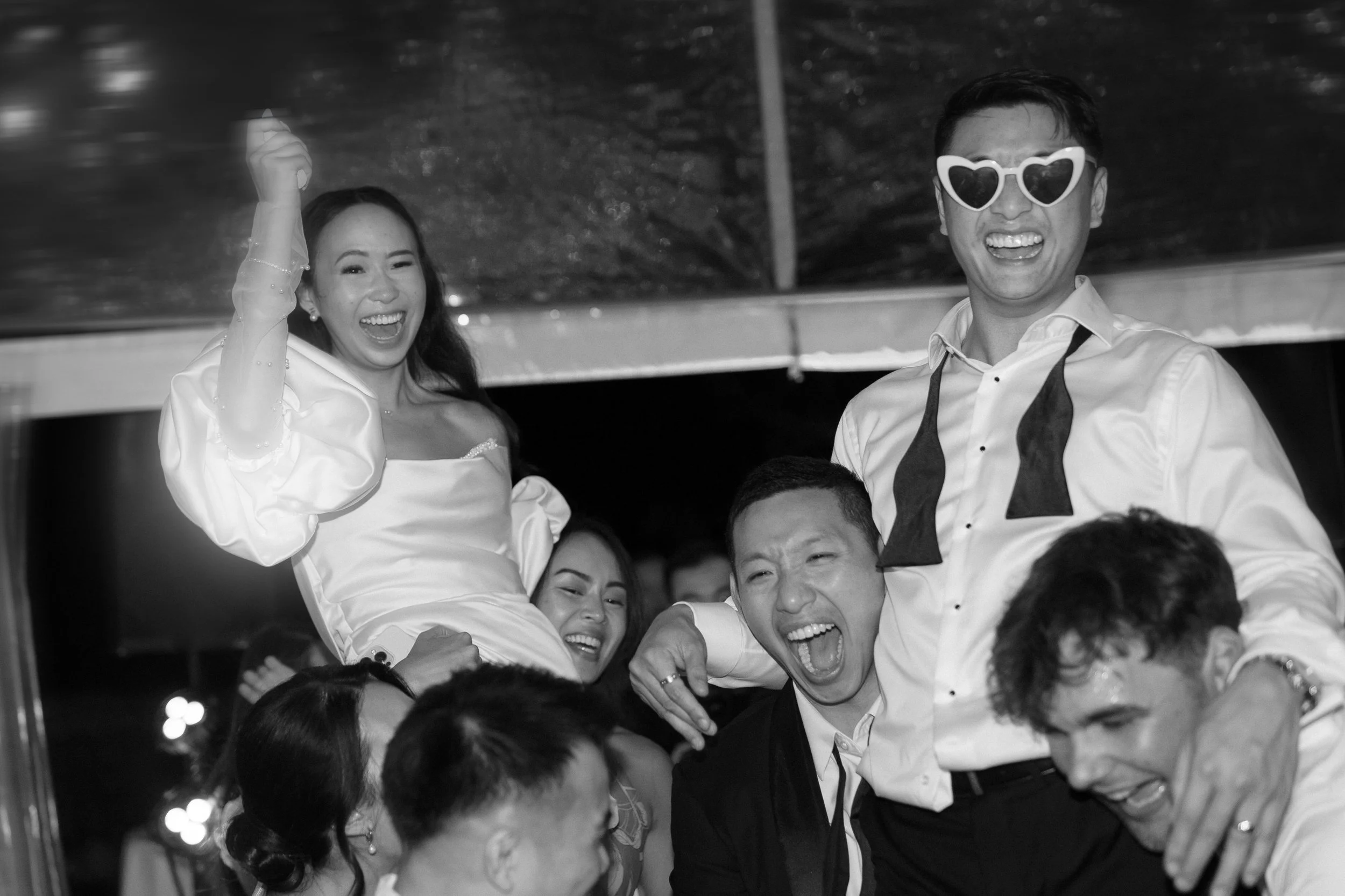 Group of friends celebrating, with some guests riding on others' shoulders, laughing and wearing party accessories, at a festive gathering.