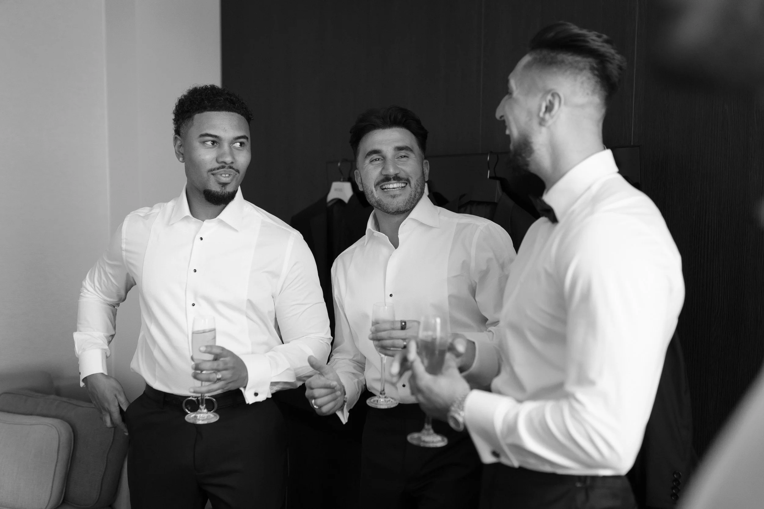 Three men in formal attire holding glasses and engaging in conversation at a social event.